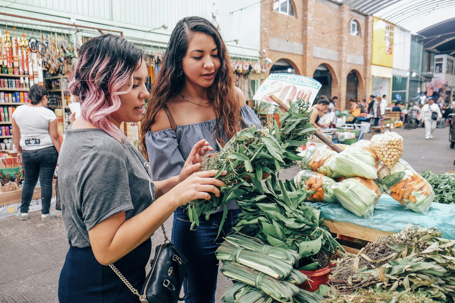 Two women friends looking at vegetables in an open-air market in Mexico City