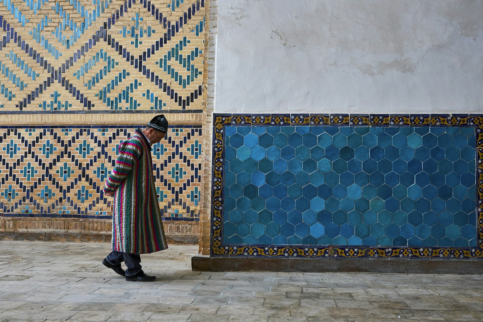 A man walks by patterned tiles in the Kalon Mosque, Bukhara, Uzbekistan