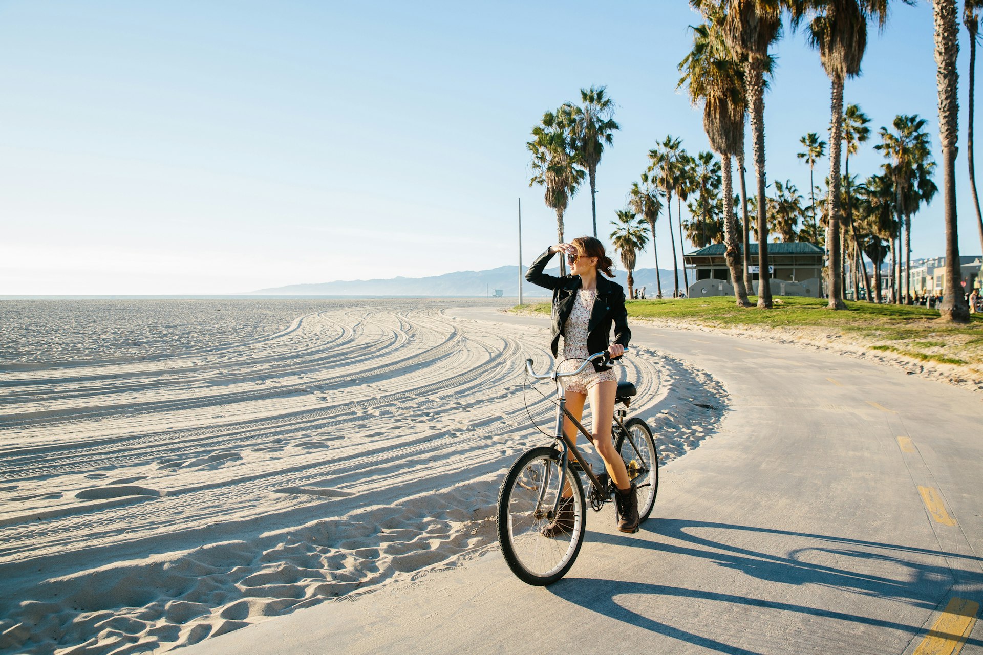 A woman cycling along Venice Beach, LA, while looking out to sea