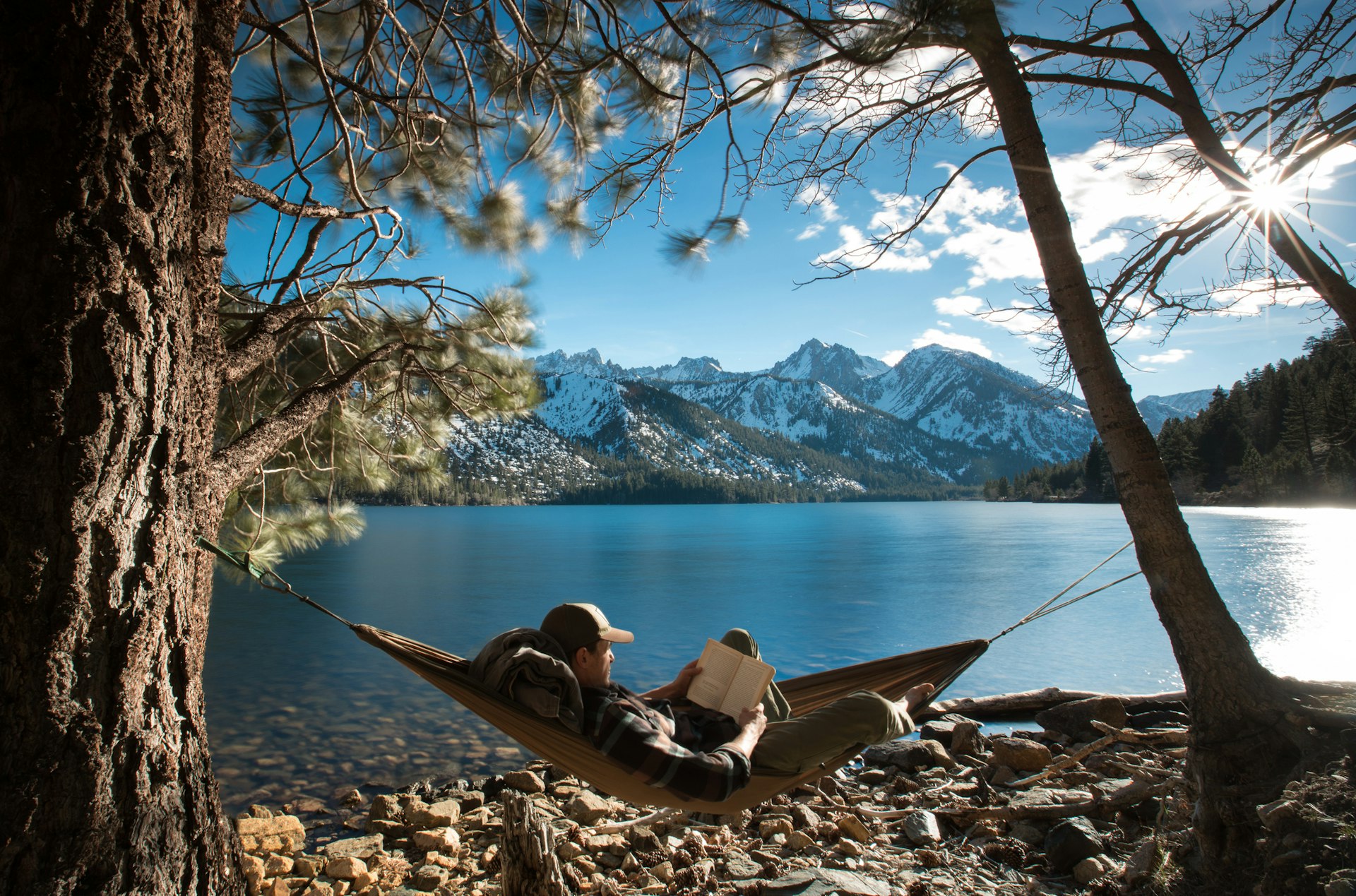 A male backpacker relaxing in a hammock next to a lake in a park in the USA