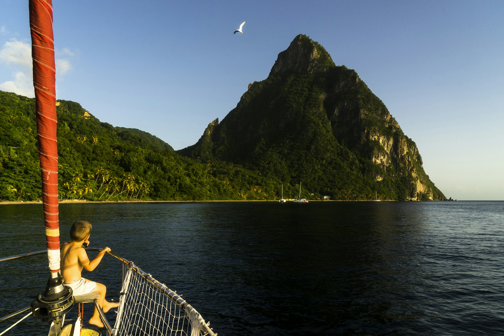 A little boy looks out of the bow of a sailing boat at the Piston Mountains in St Lucia