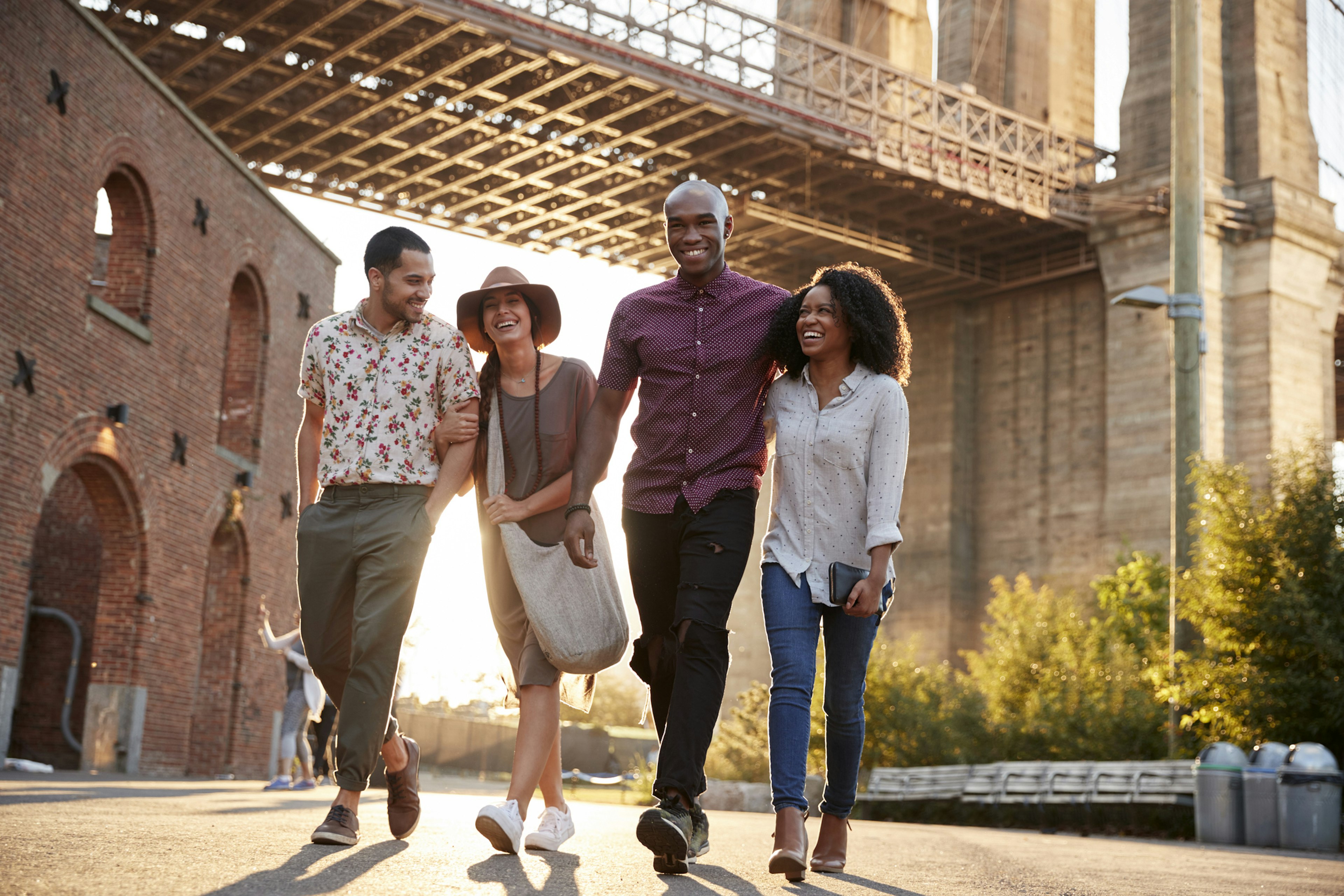 Four friends walking and laughing together under the Brooklyn Bridge