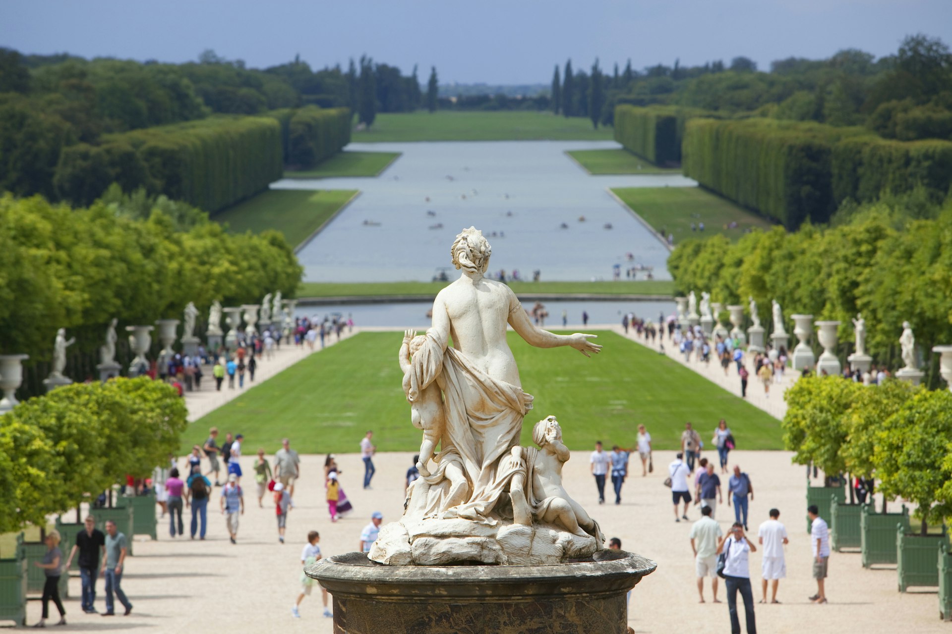 A rear view of a statue and crowds in the distance in the gardens of Versailles Palace, Versailles, France