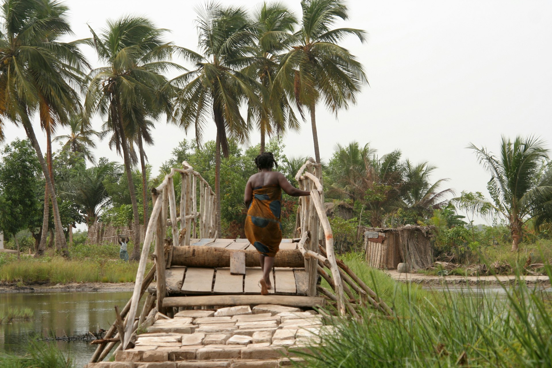 A woman walks across a wooden bridge in Oidah, Benin