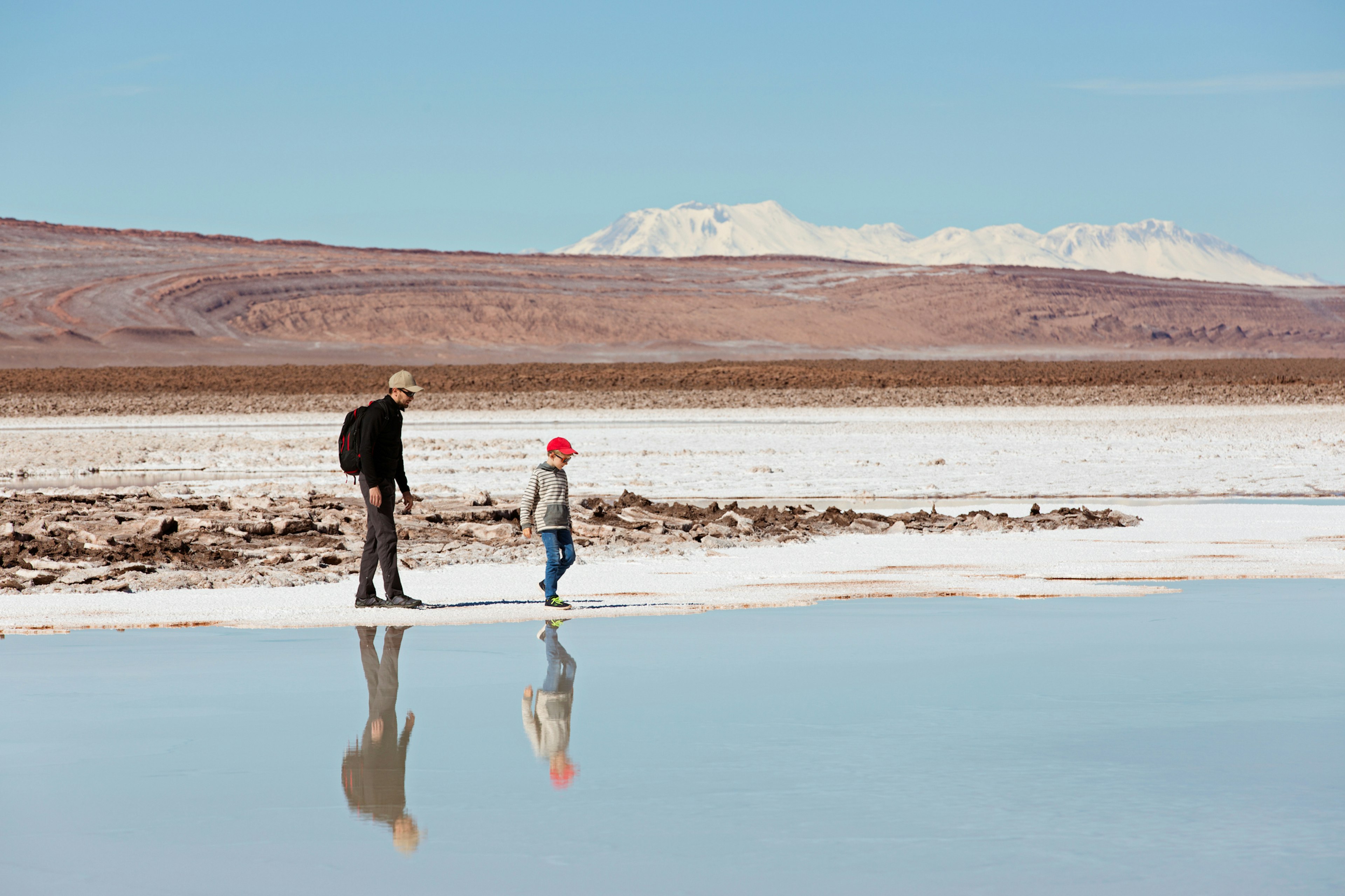 A father and son walk along beside a salt lake in a vast desert landscape