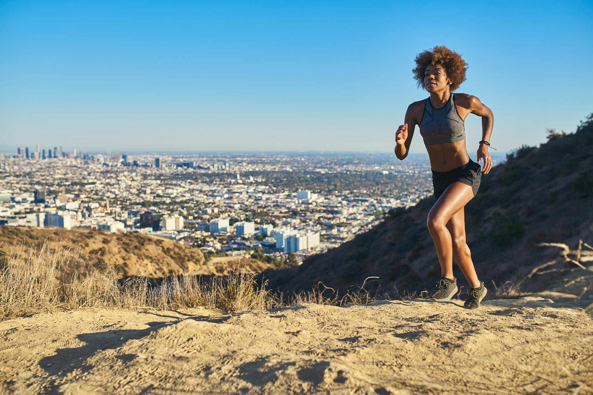 A woman runs up a path at Runyon Canyon with Los Angeles in background