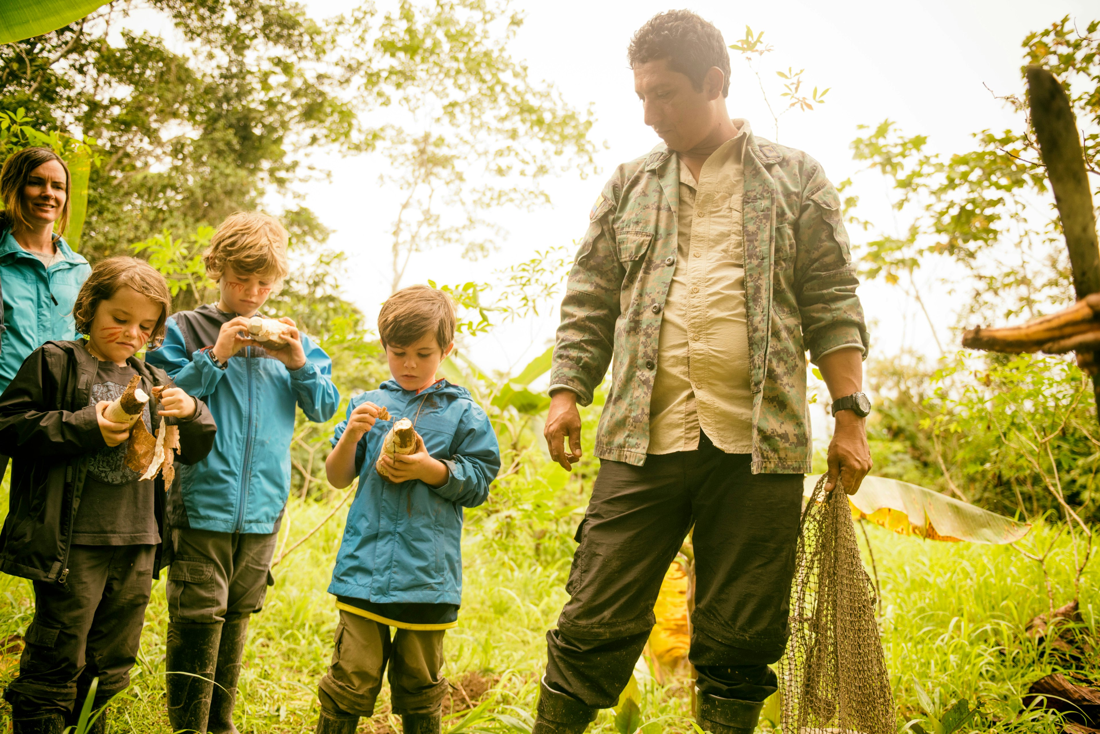 Three kids look at yucca roots alongside a guide in the Ecuadorian Amazon