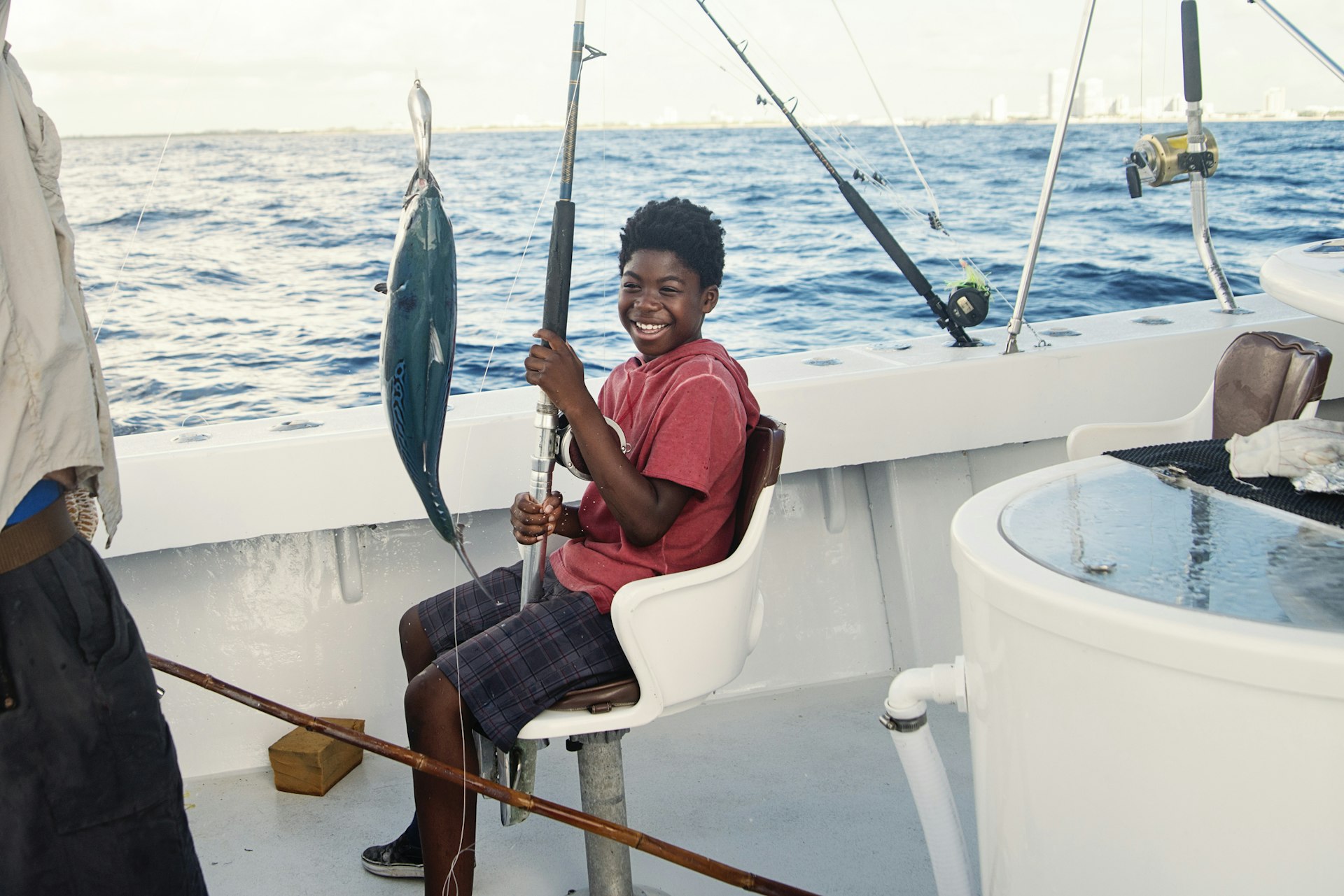 A preteen boy smiles as he catches a fish out on a boat that's gone deep-sea fishing