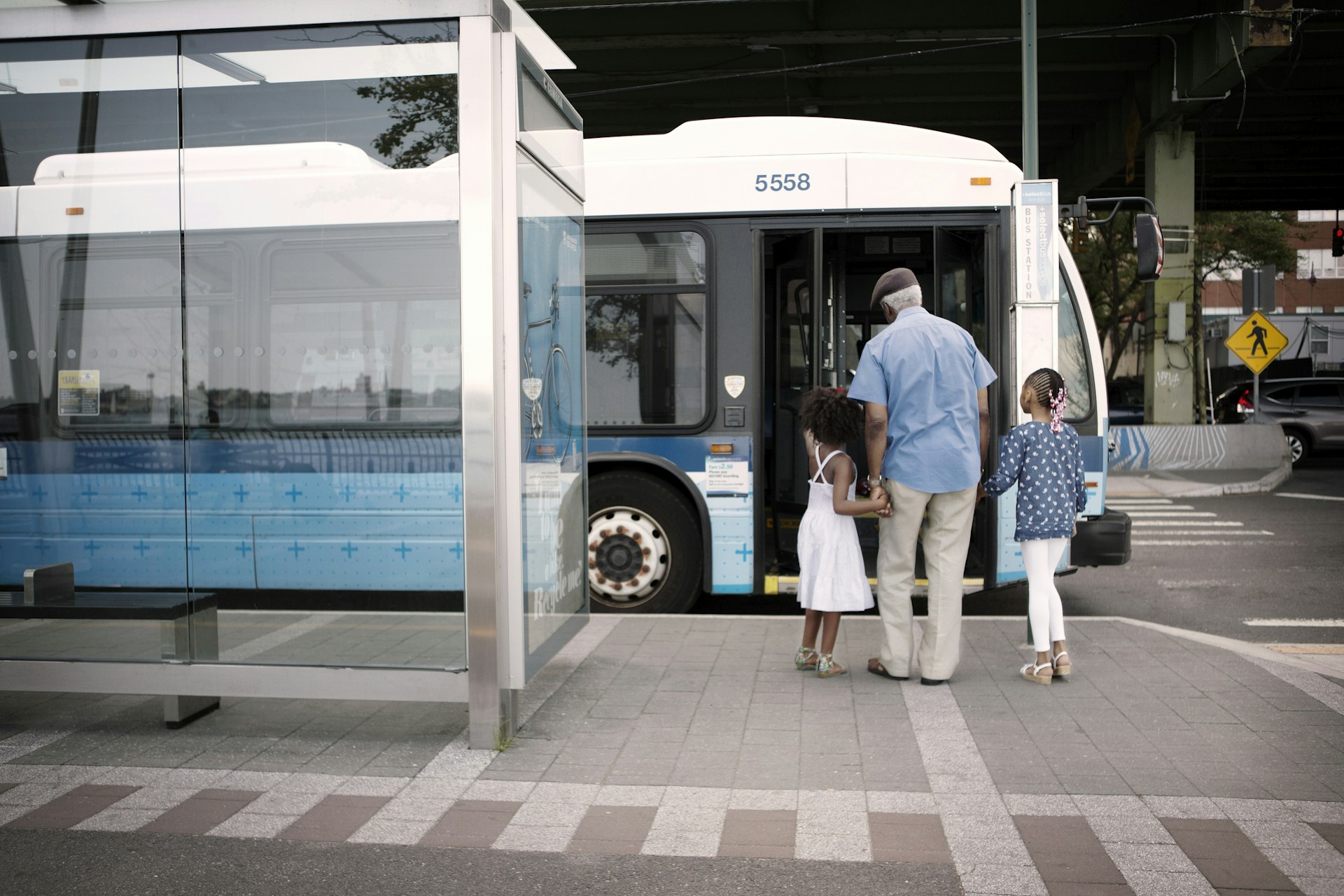 A grandfather and his two grandkids holding hands and boarding a city bus together 