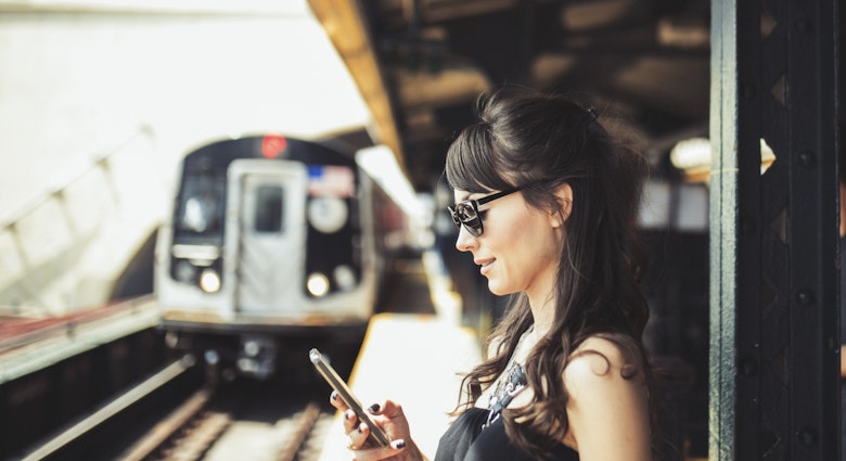 A woman waiting on a platform looking at her phone as a train comes into the station.