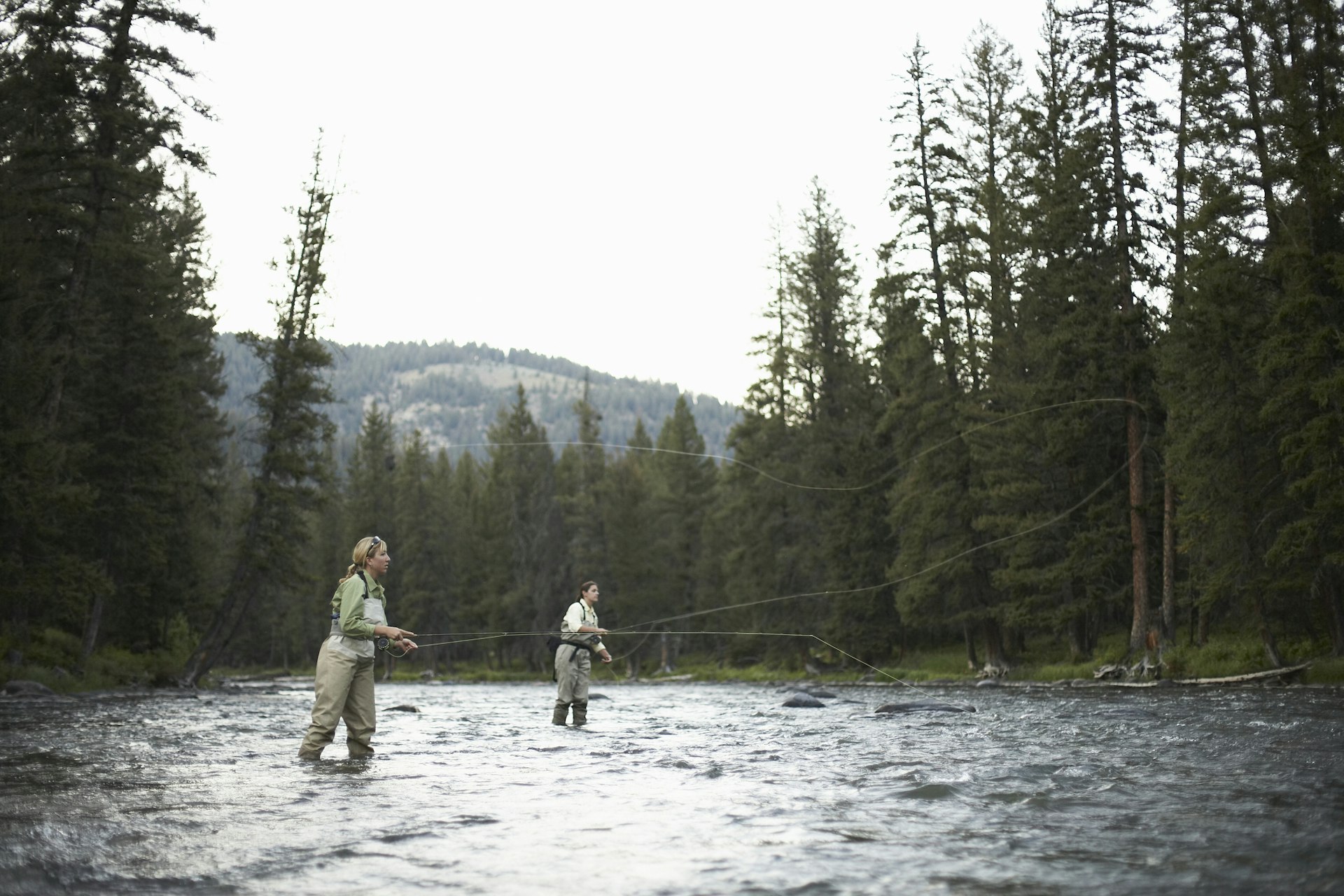 Two anglers in waders cast off as they fly-fish in a river