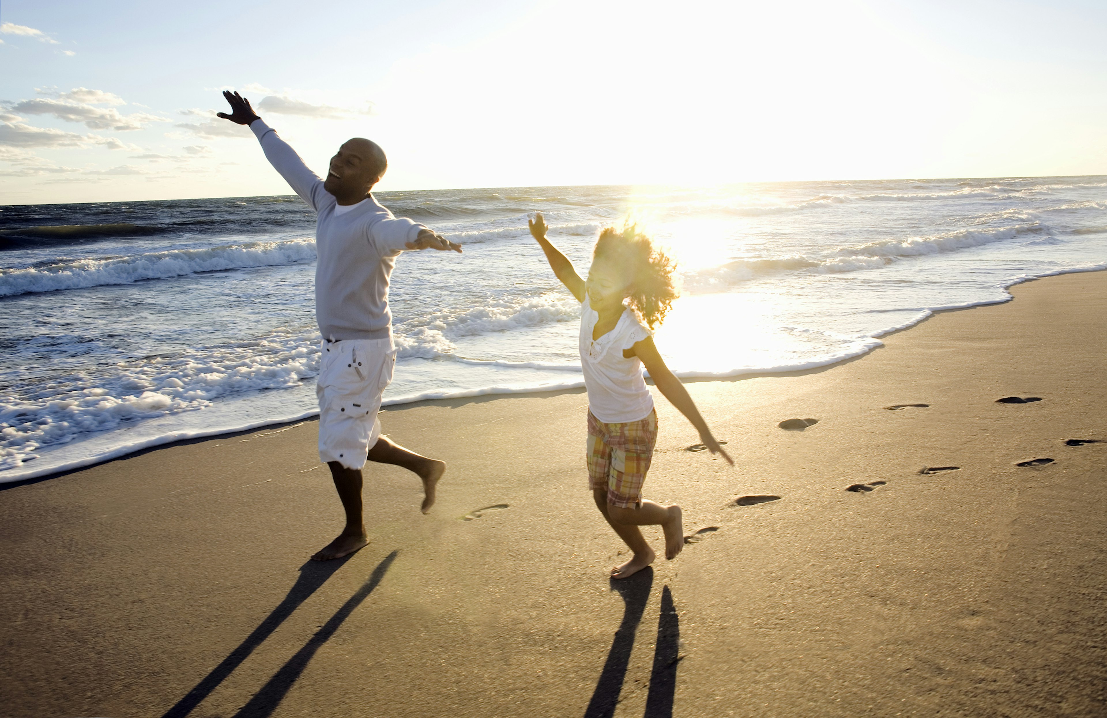 A man and his daughter running along a beach in Florida with arms outstretched