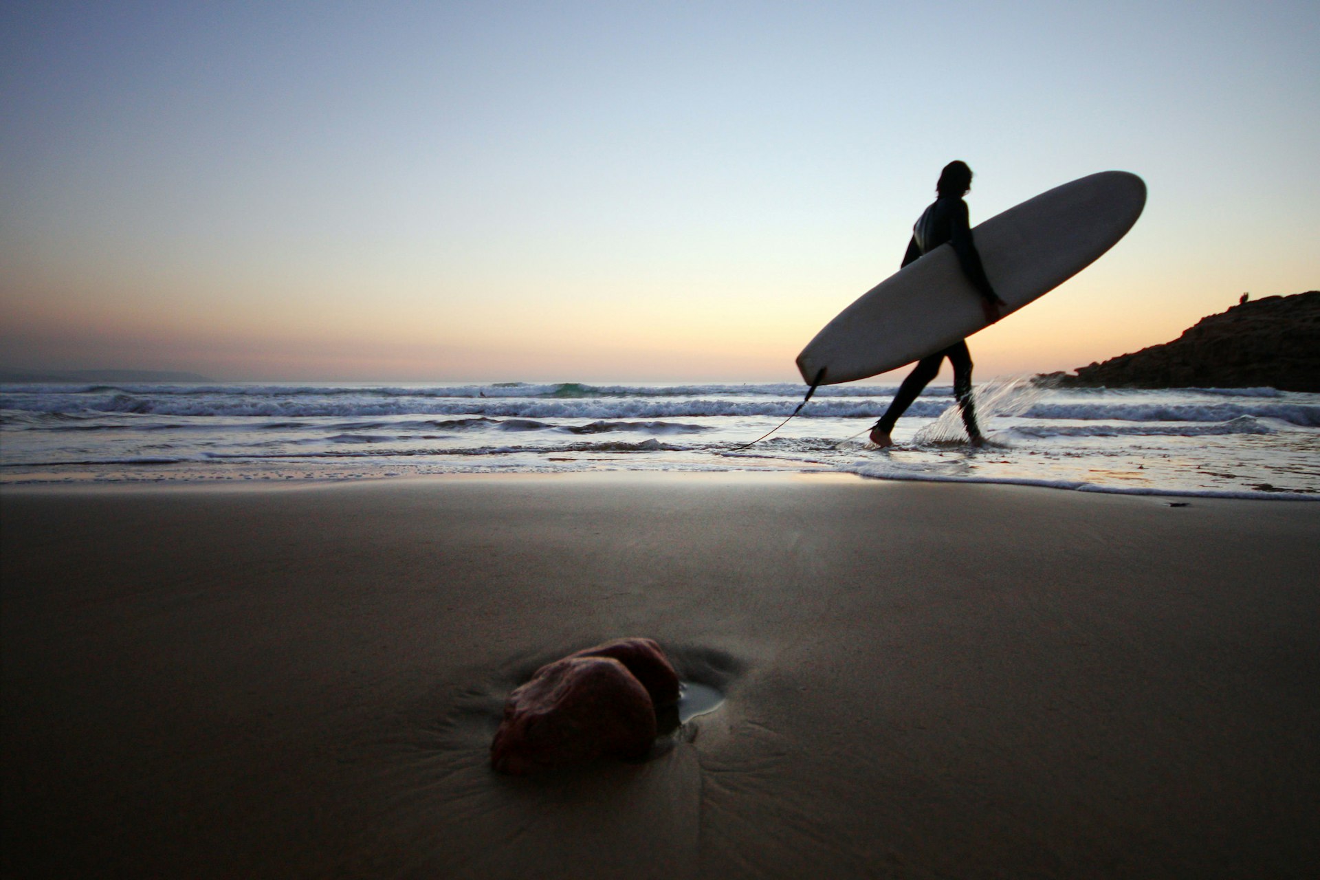 A surfer on the beach at sunset in Taghazout, Morocco