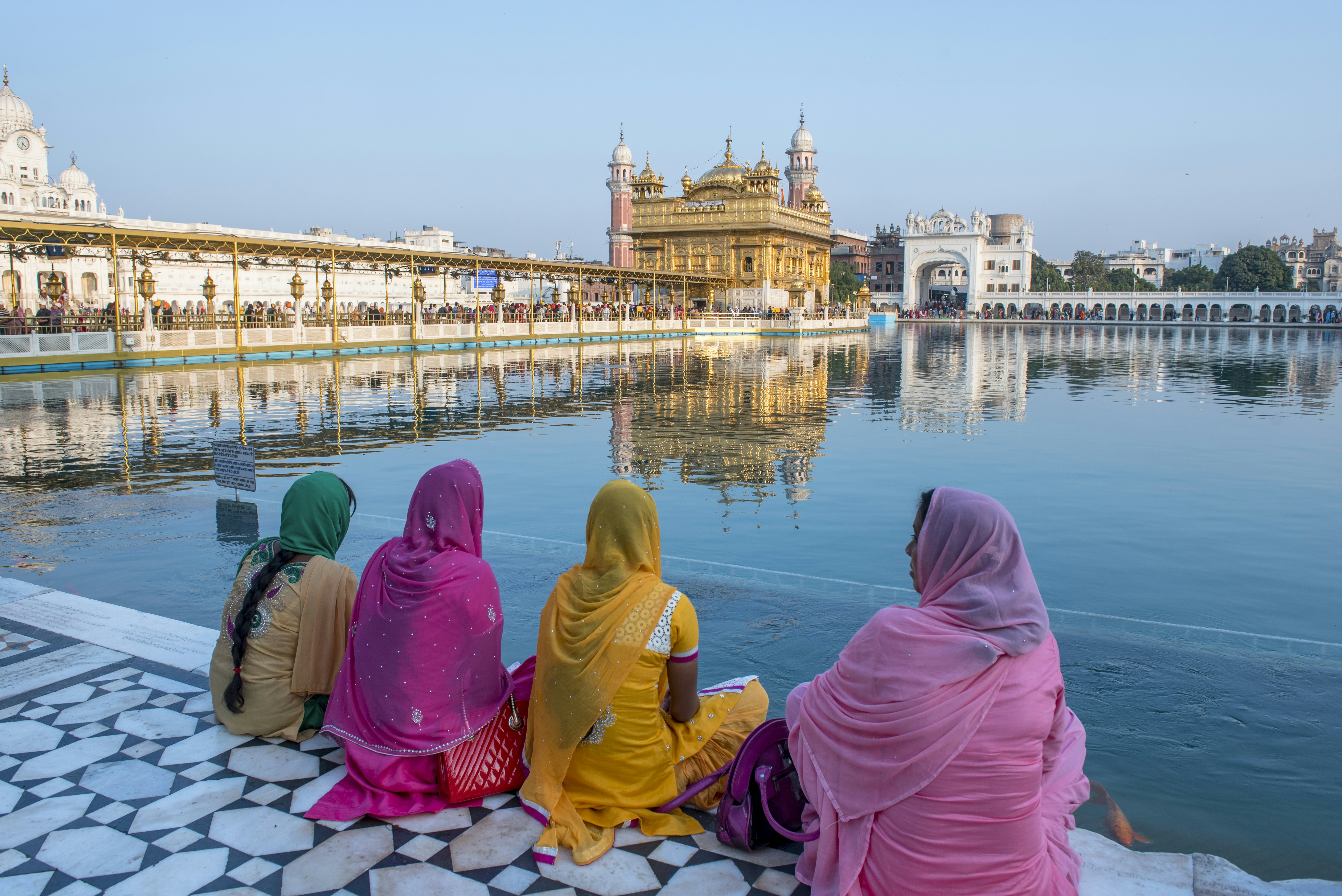 Women in traditional costume sitting on the bank of pool surrounding the Golden Temple, Amritsar, India