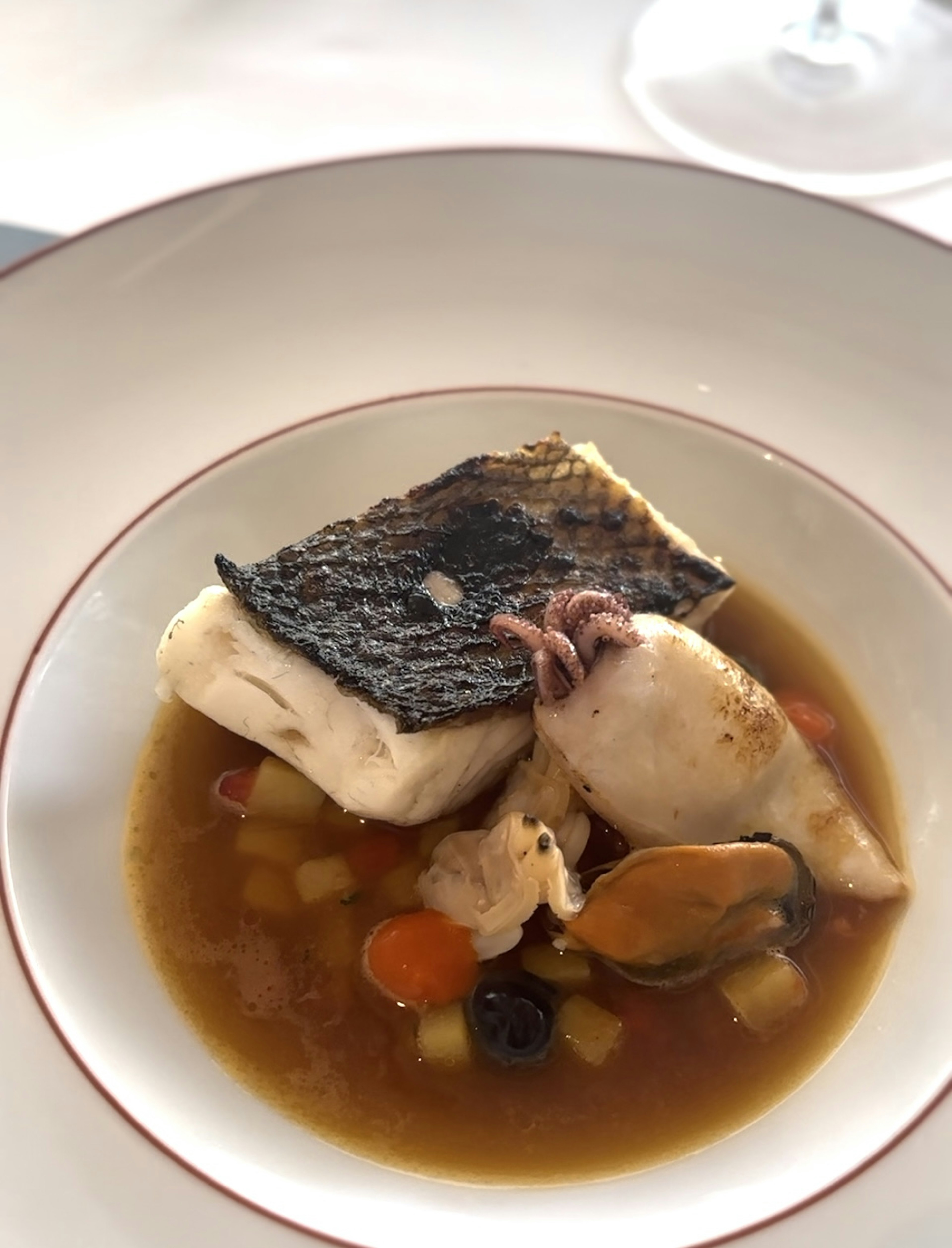 A white bowl serving a trout and octopus soup