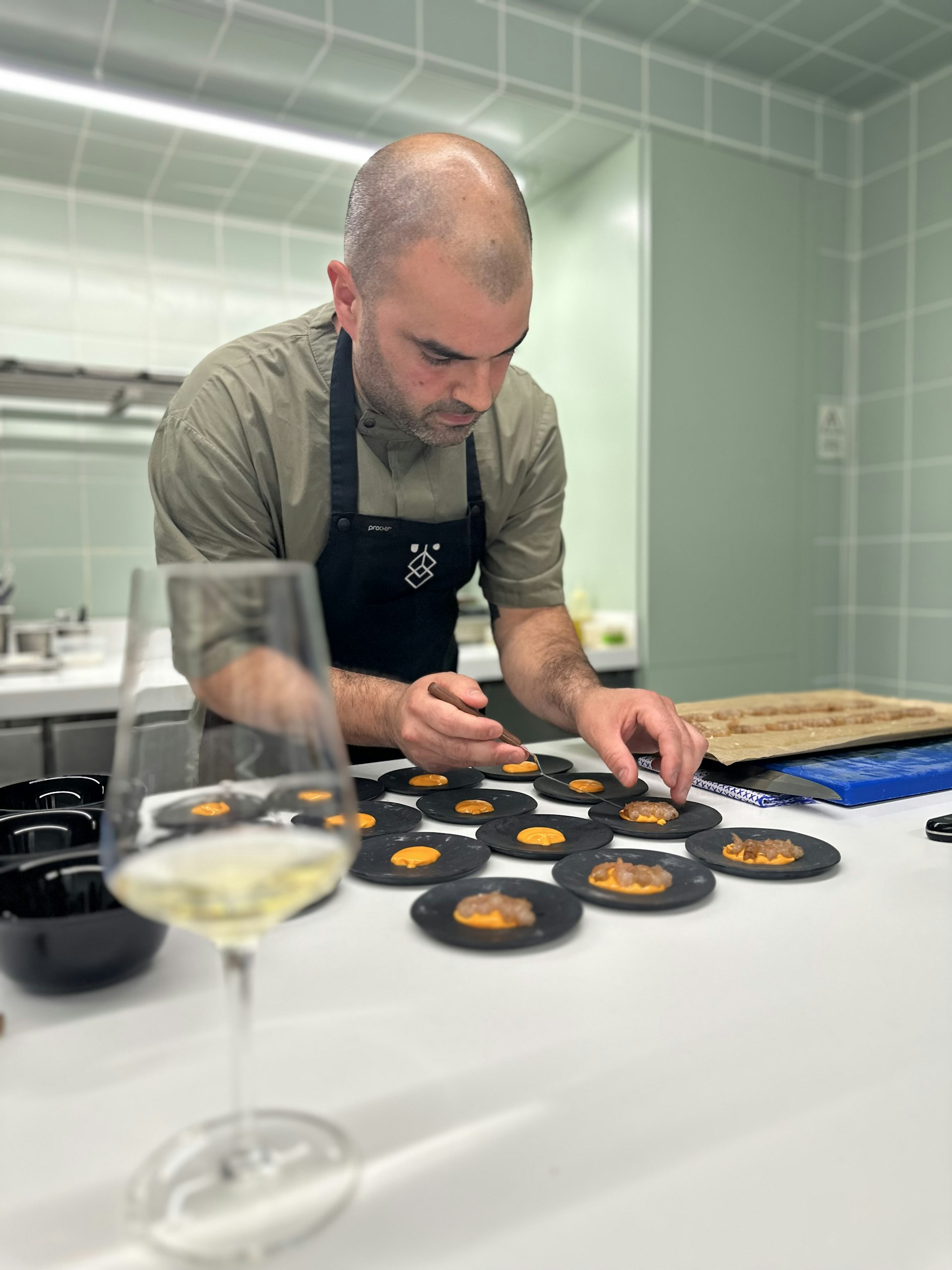 A chef prepares tiny dishes on small round black plates in a fine dining restaurant