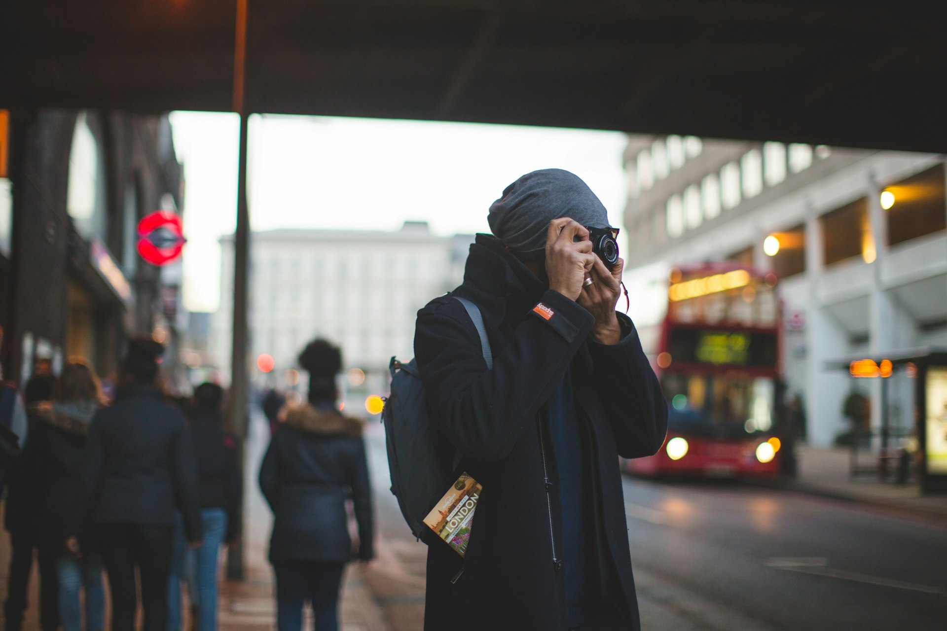 Man takes a photo in a London street with red bus in background