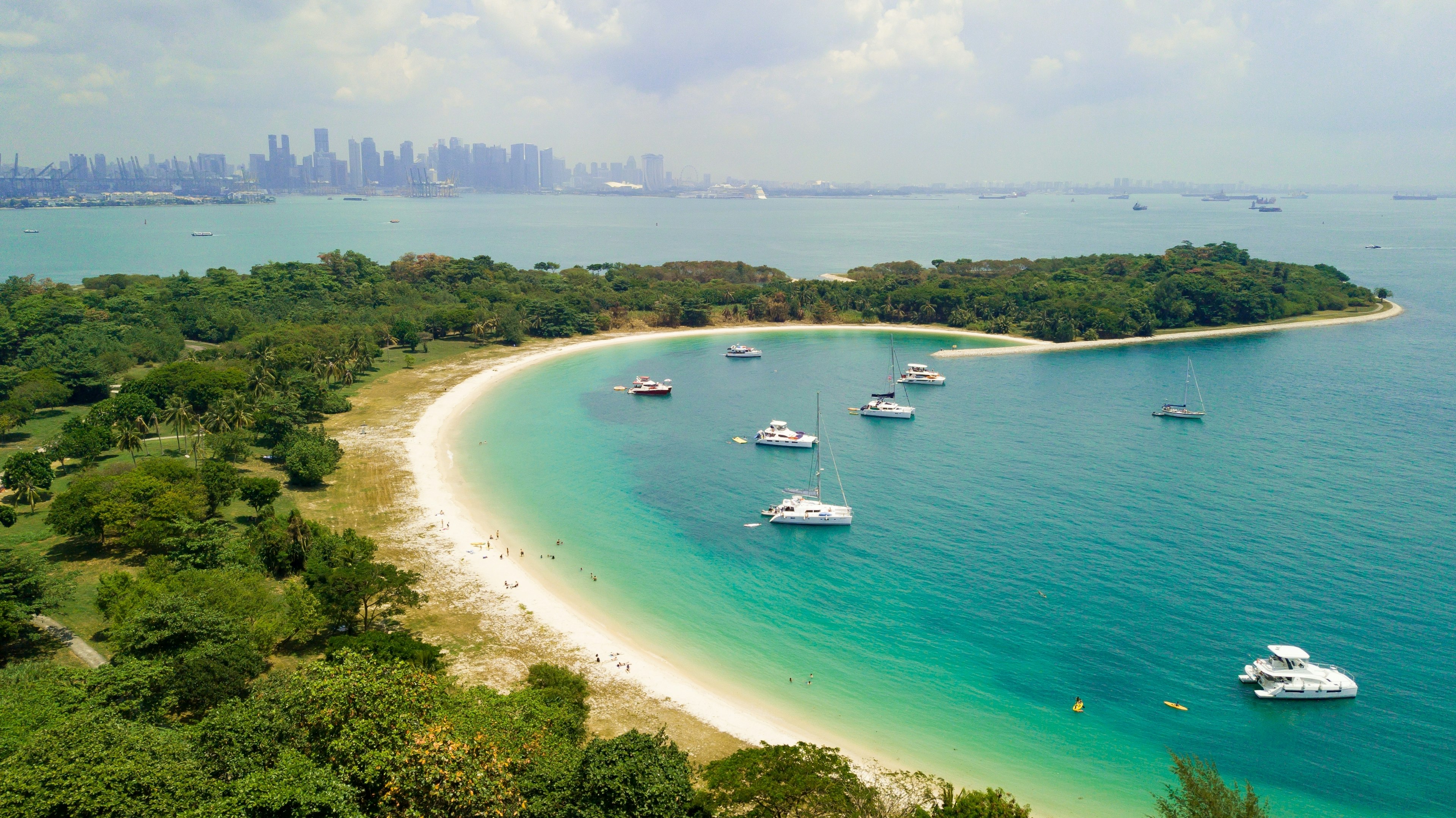 A lovely arc of golden sand with a few boats docked in the ocean. A city skyline rises in the distance