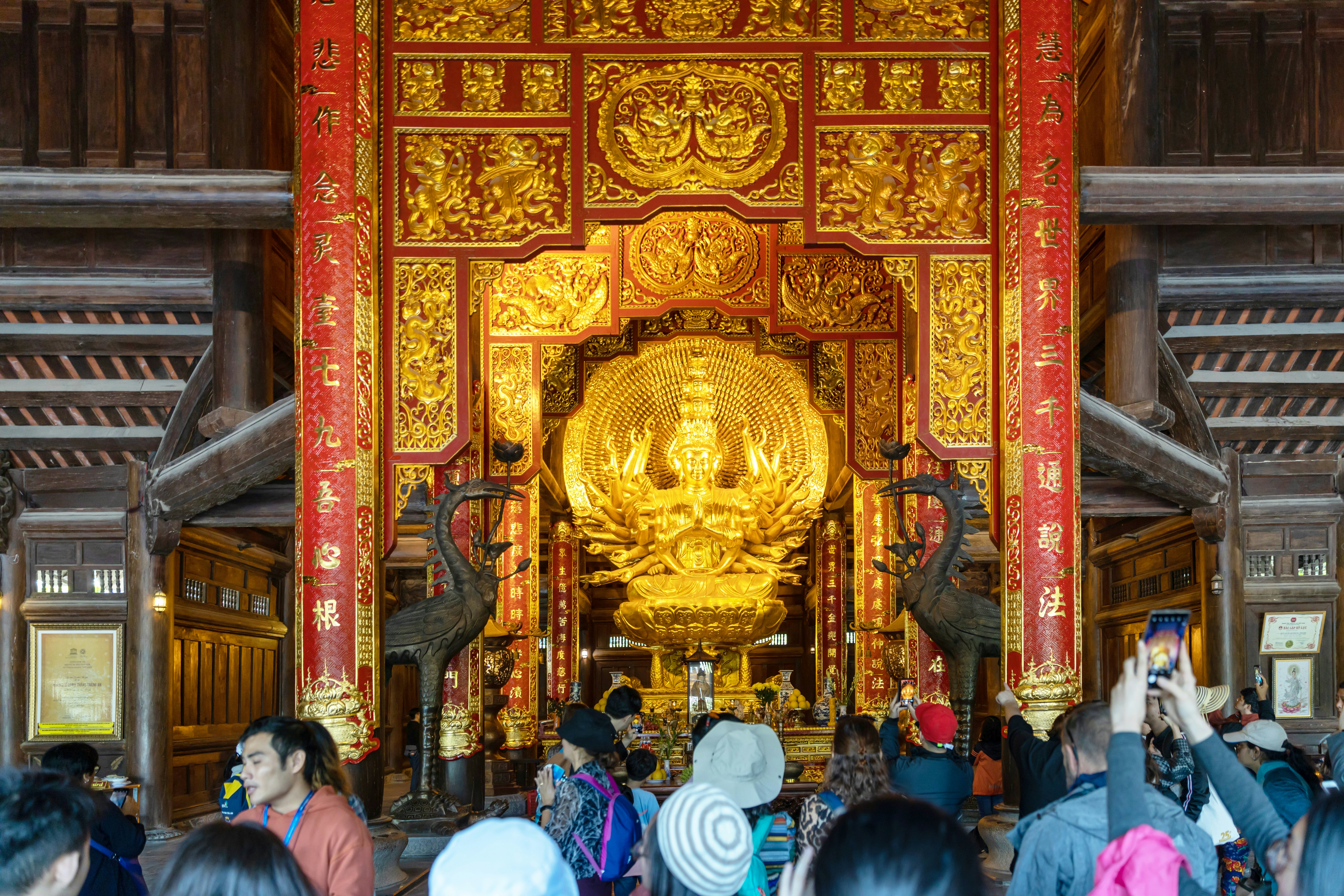 People crowd in front of an altar featuring an ornate sculpture of the Buddha and a screen at a public temple