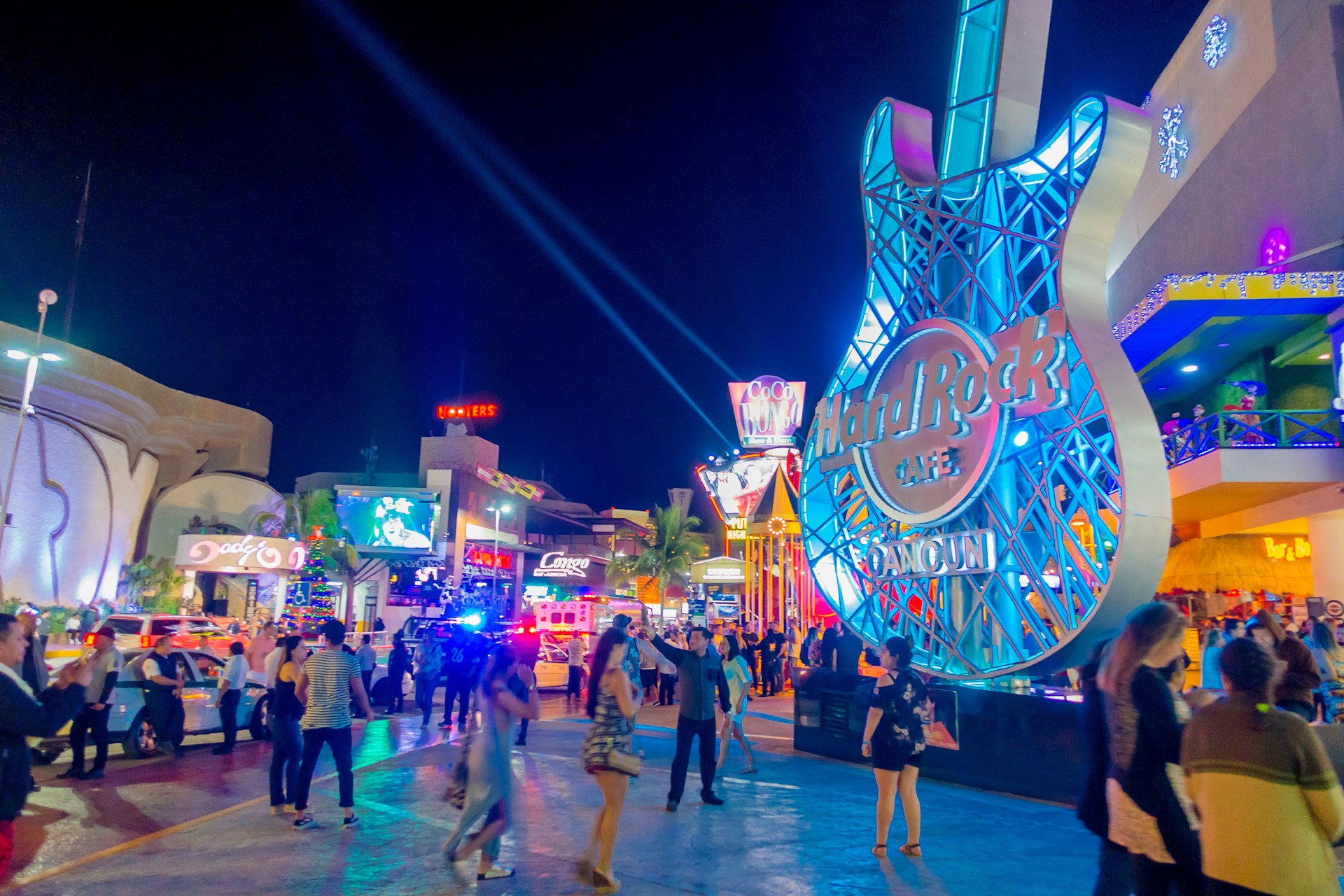 Crowds of people in the street outside neon-lit restaurants and bars