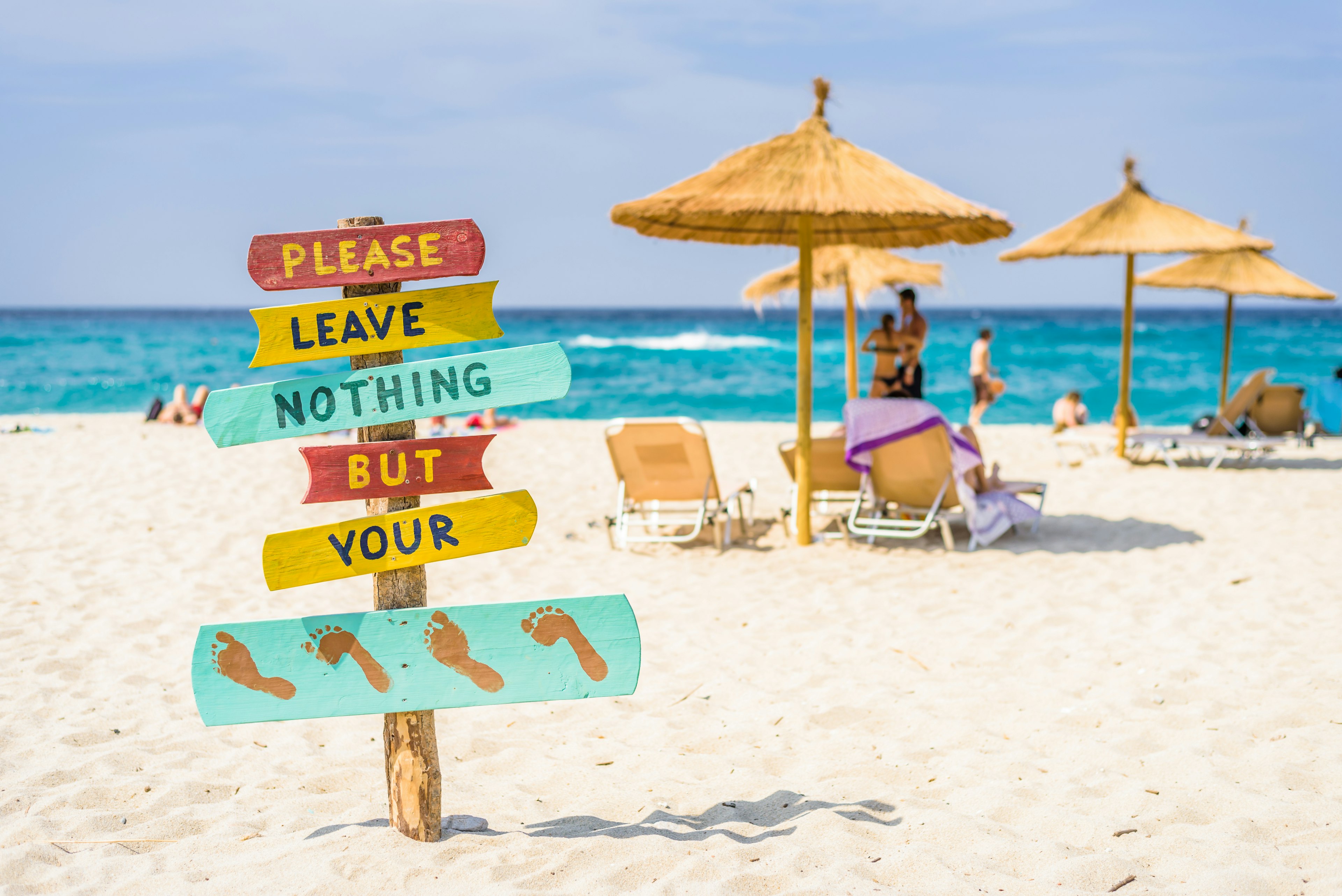 The golden sand on Livadhi Beach near Armenistis on Ikaria island, Greece. A sign asks visitors to leave nothing but footprints behind.