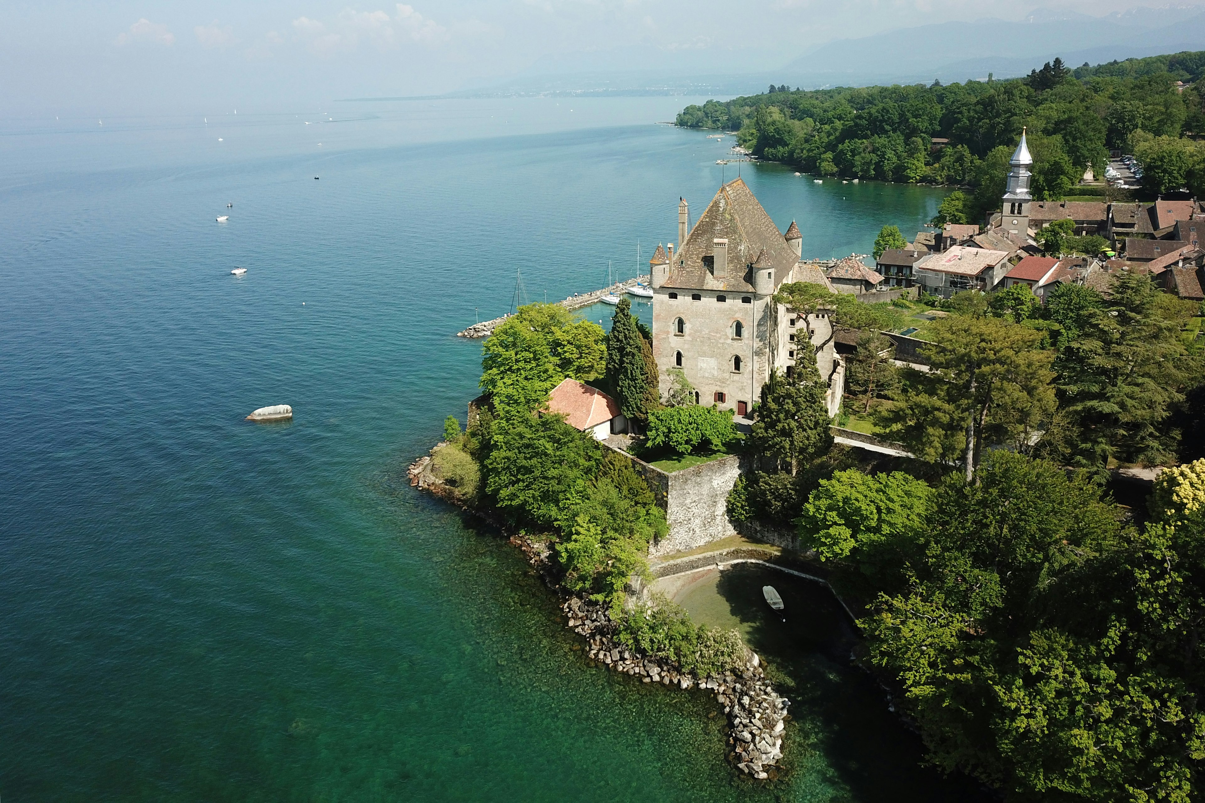 An aerial view of a stone castle on the shore of a turquoise Lake Geneva