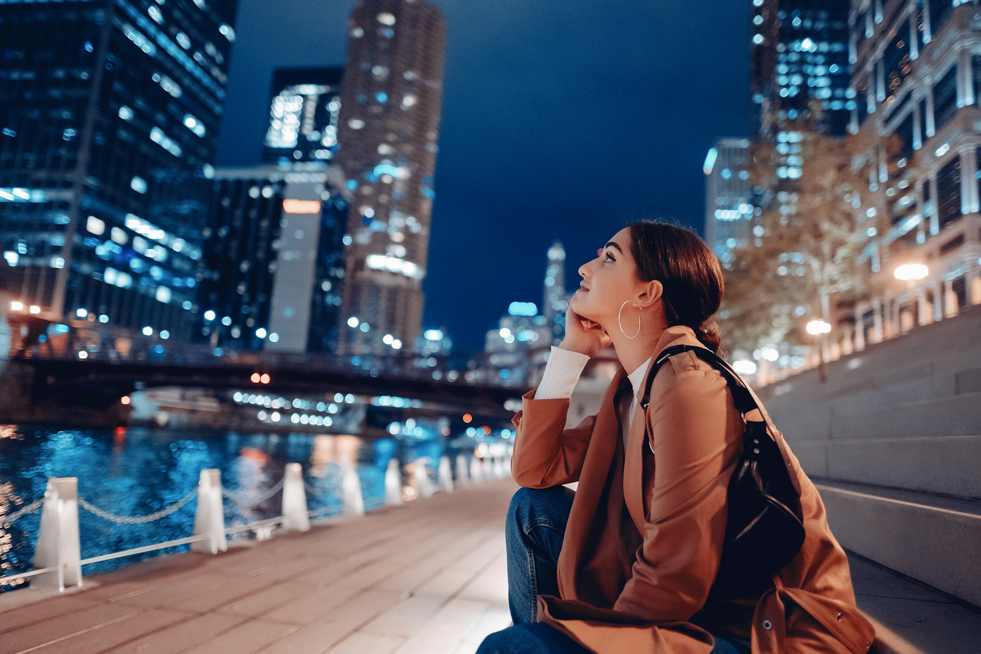 Young woman sitting near the Chicago River at night looking at skyscrapers, Chicago, Illinois, USA
