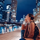 Young woman sitting near the Chicago River at night with skyscrapers © Oleggg / Shutterstock