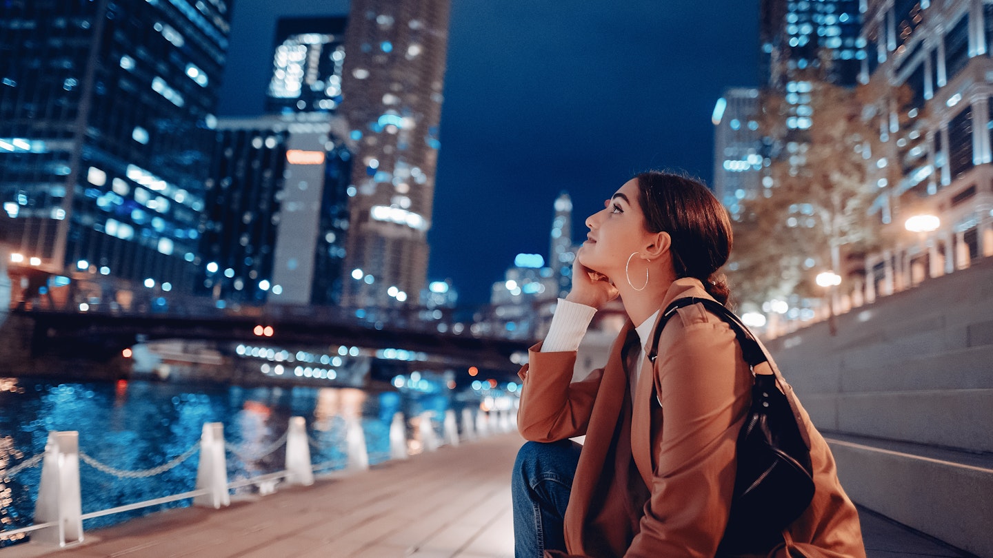 Young woman sitting near the Chicago River at night with skyscrapers © Oleggg / Shutterstock