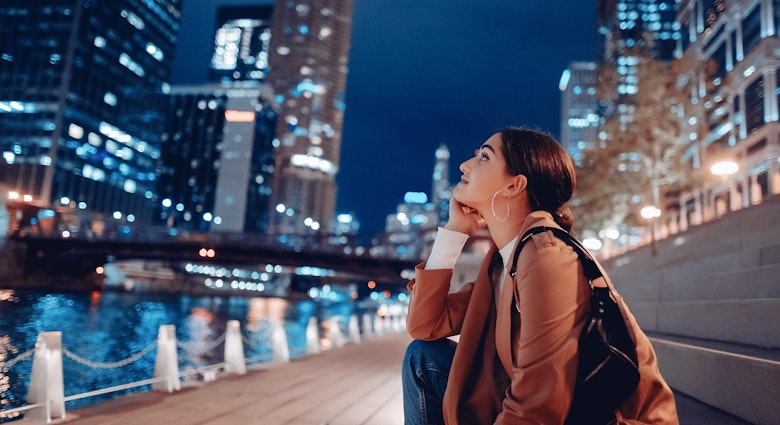 Young woman sitting near the Chicago River at night with skyscrapers © Oleggg / Shutterstock