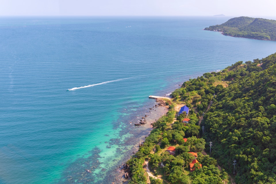 View over Hon Thom Island coast from Phu Quoc cable car with a speed boat down on the sea and rainforest with som small hauses and the horizon in background.
