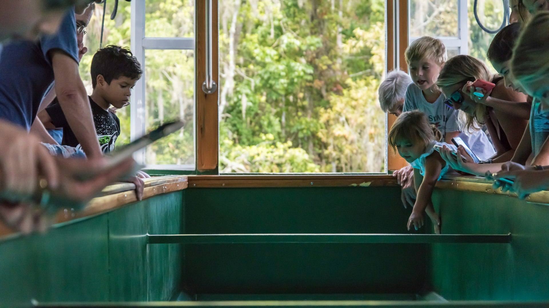 A group of kids gather round railings at the center of a boat so they can gaze through the glass-bottom below