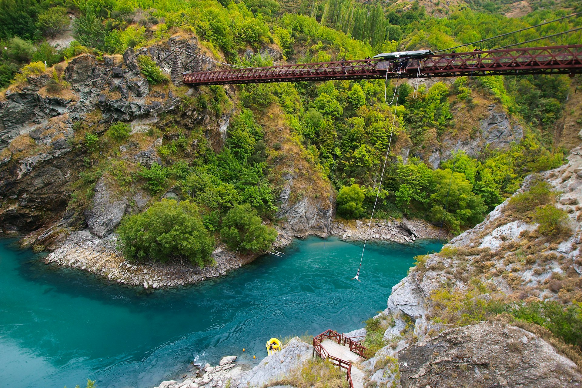 Bungy jumper plunges off a bridge towards an alpine river that flows below