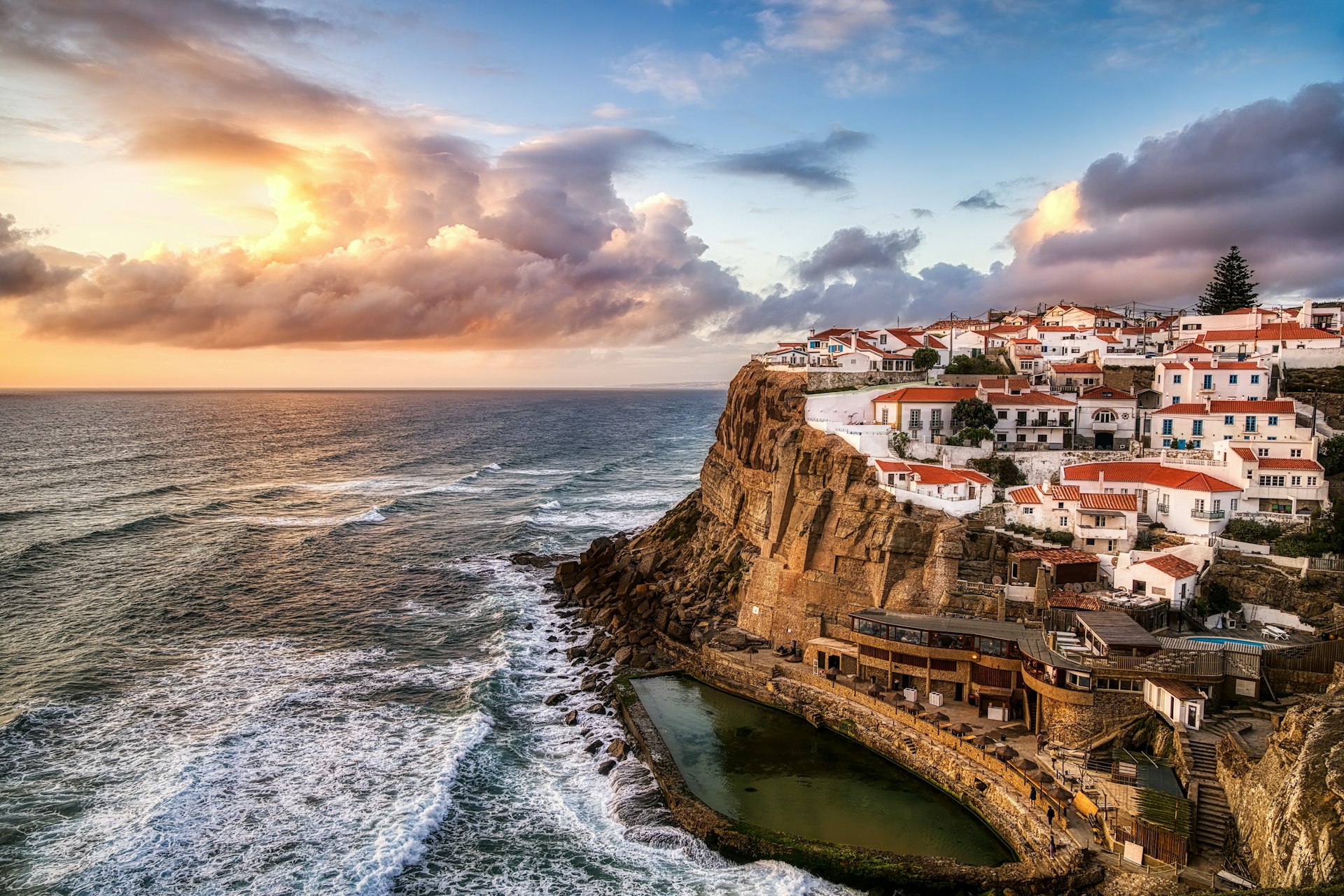 A cliffside view of white houses along a craggy coastline in Sintra at sunset