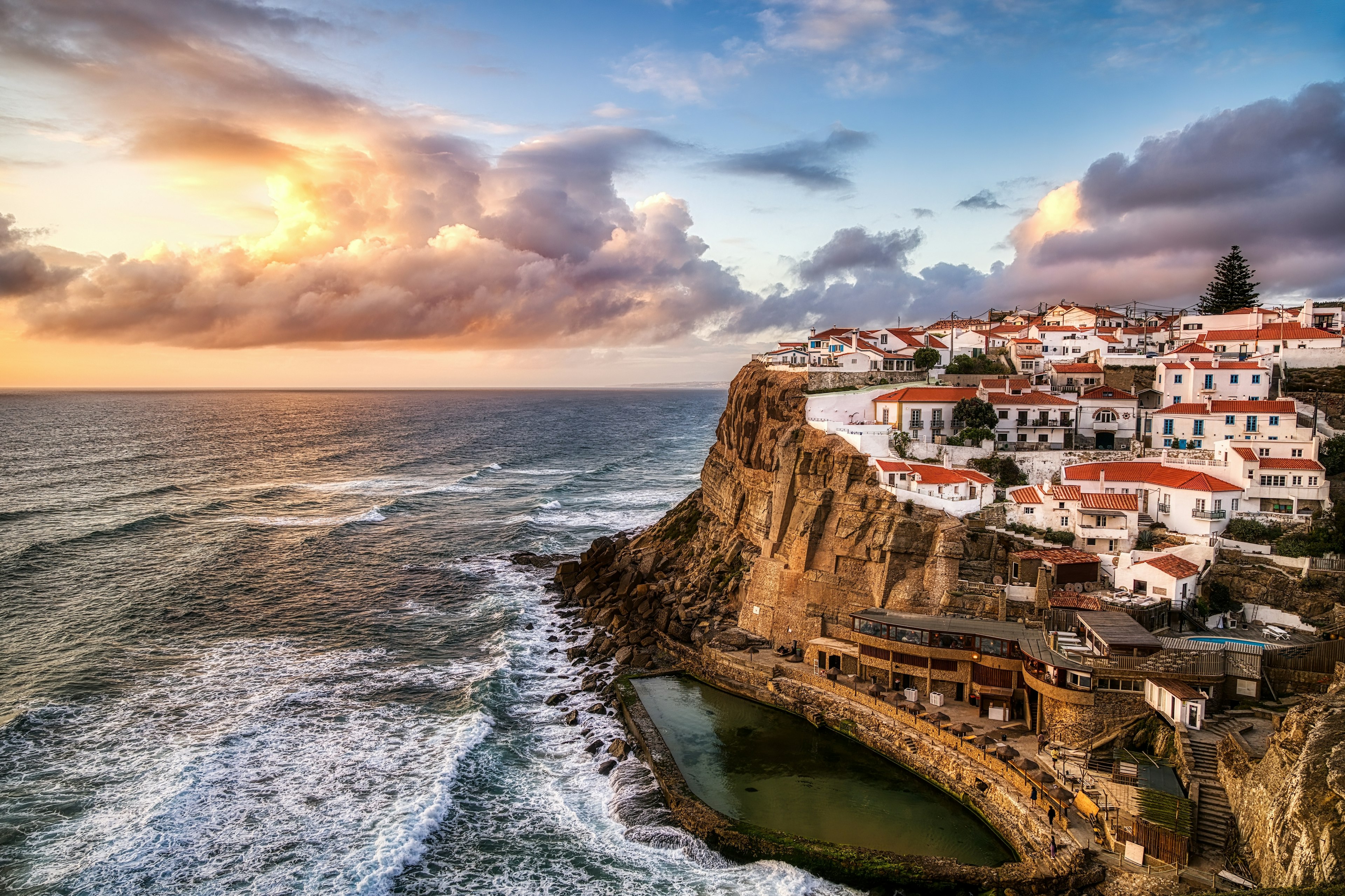 A cliffside view of white houses along a craggy coastline in Sintra at sunset