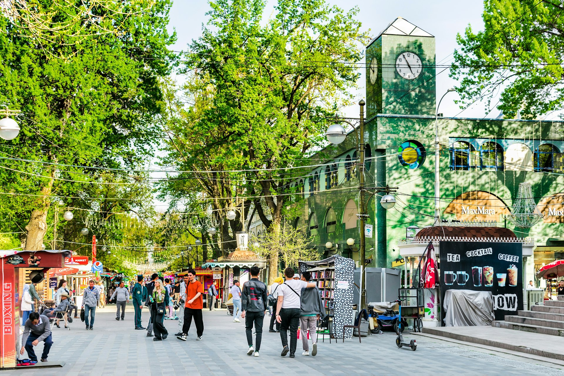 People walk down a tree-lined pedestrianized street lined with kiosks and stalls