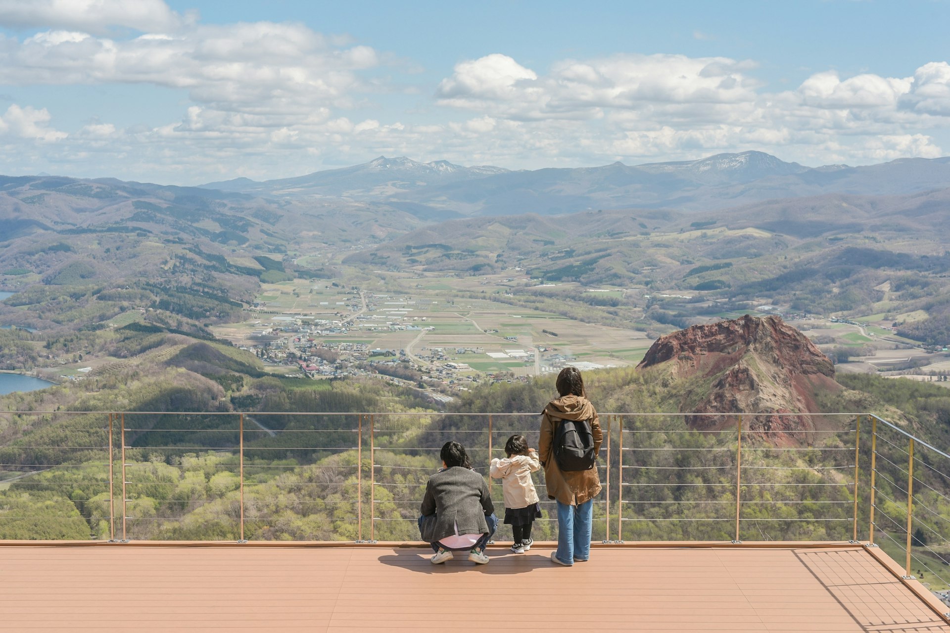 A small family group look out over a vast landscape from a viewpoint