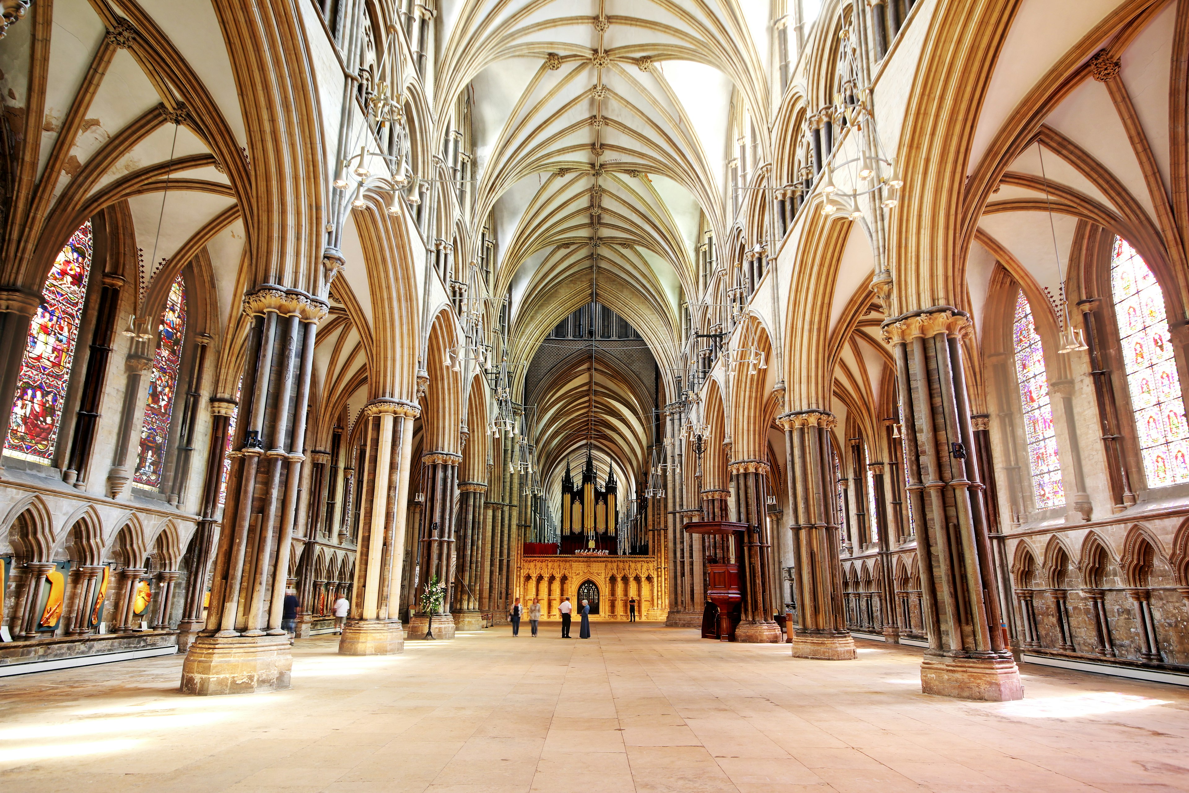 The nave of a vast cathedral with many arches and flying buttresses. Some people are standing there, seeming very small in the huge space