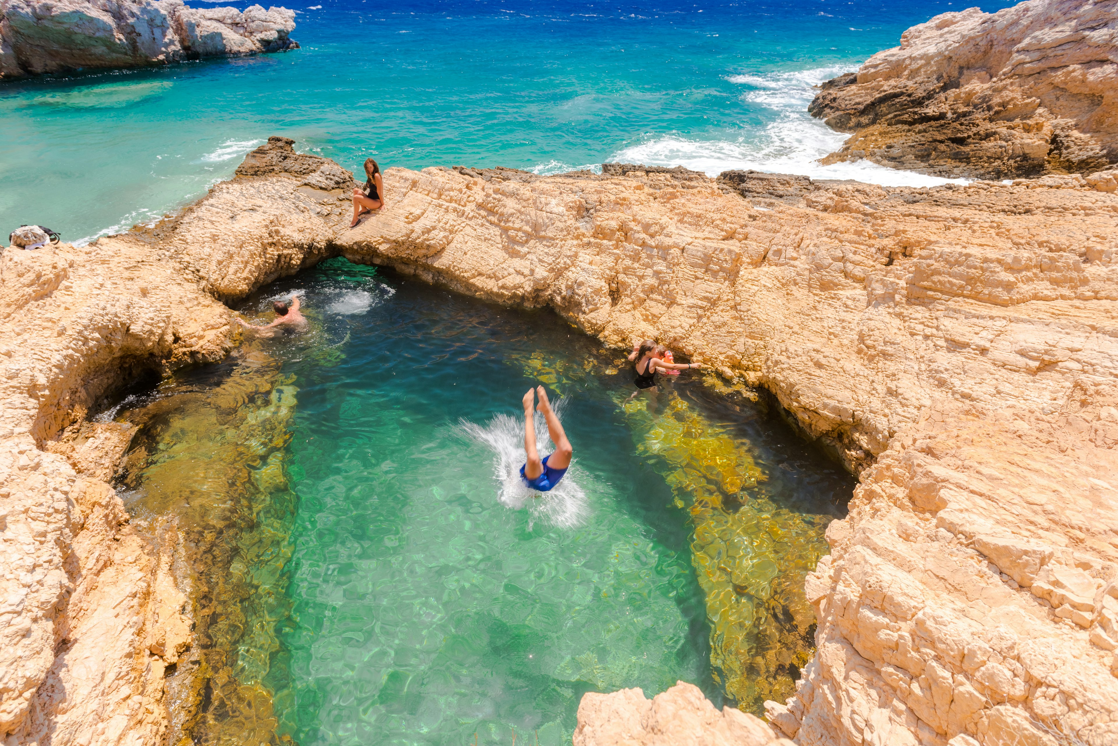 People dive into a natural pool in rocks on the shore