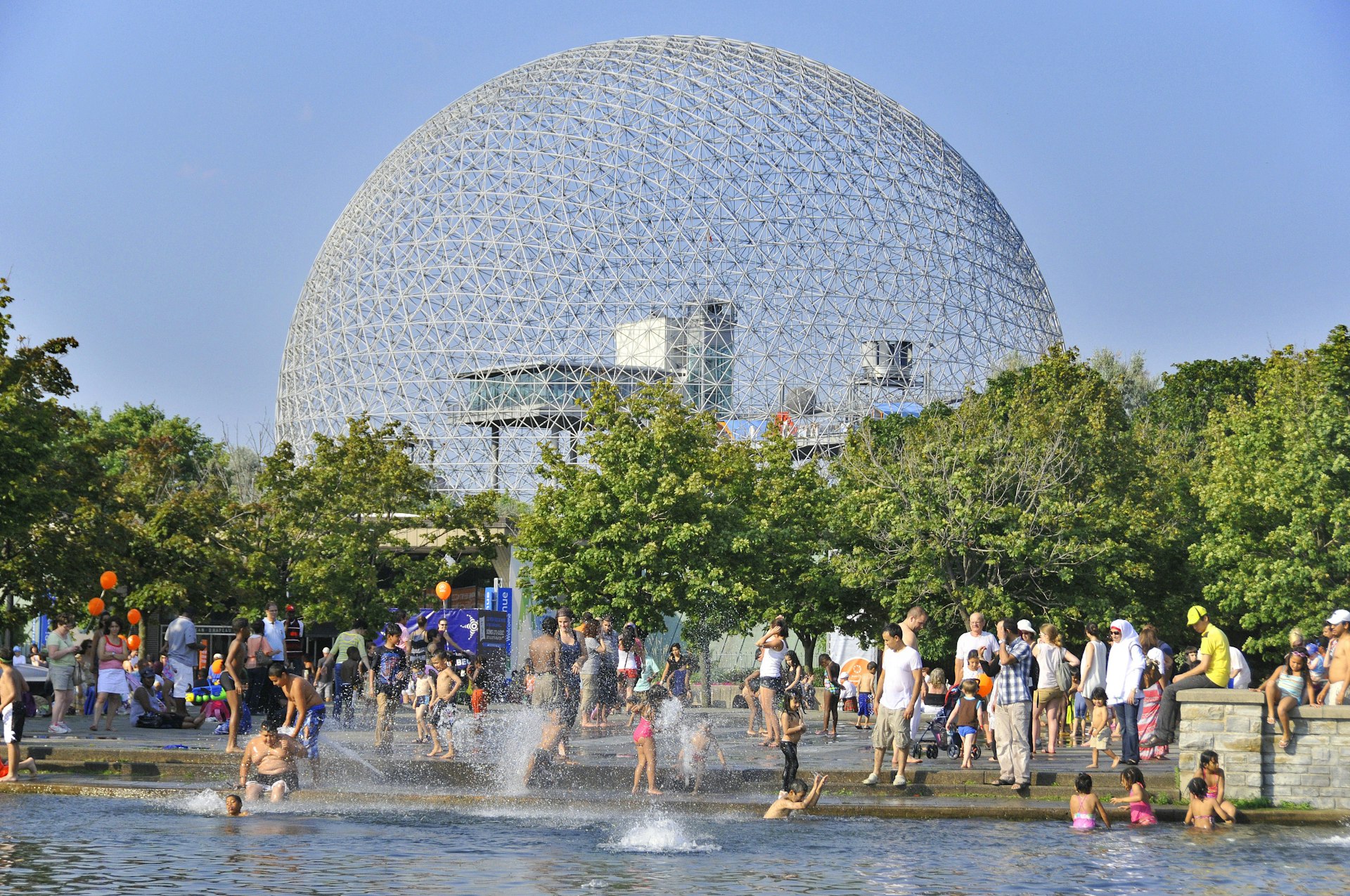 Kids and families play in water fountains near a vast dome-like structure