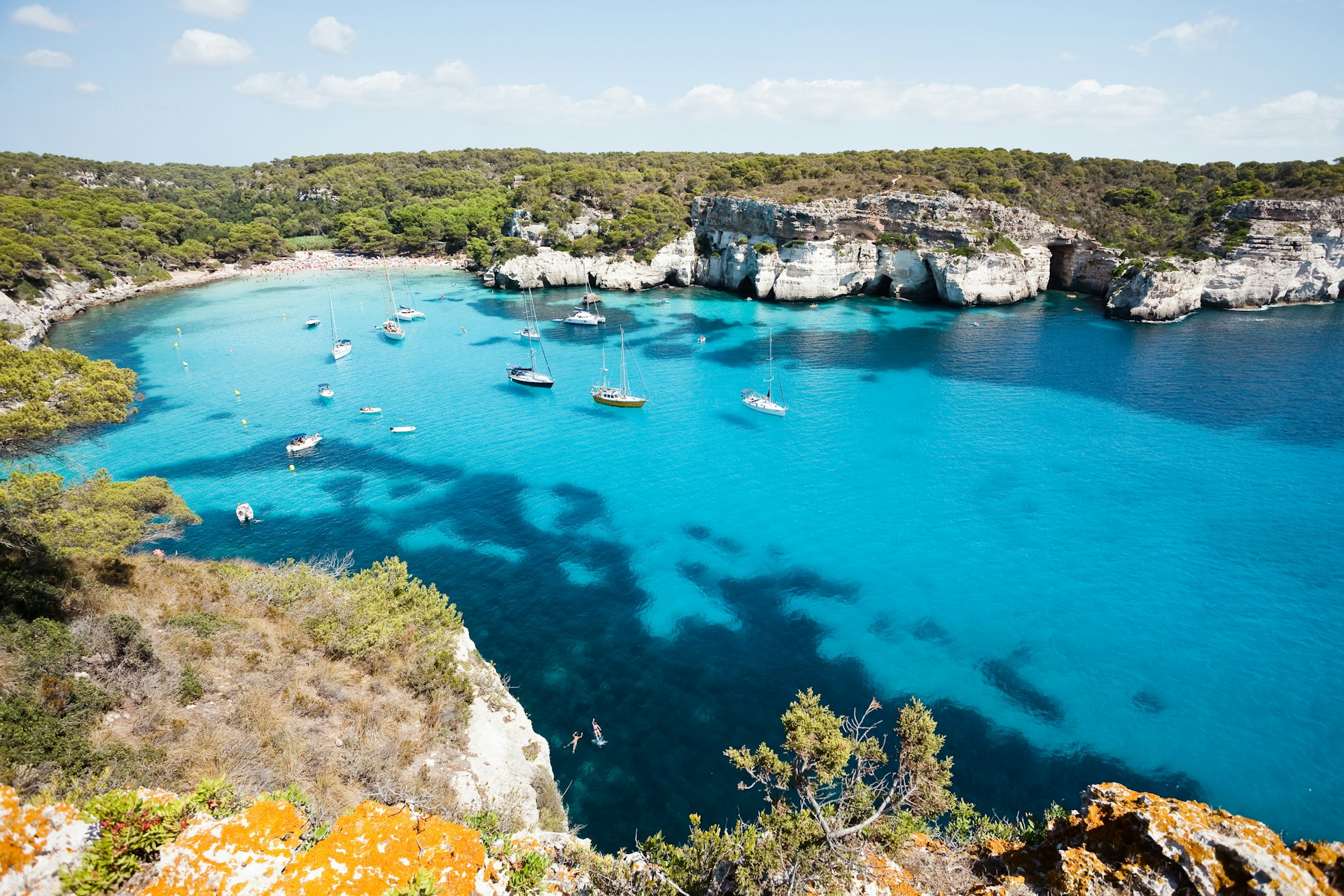 Boats float on bright blue waters off the coast of Menorca. 