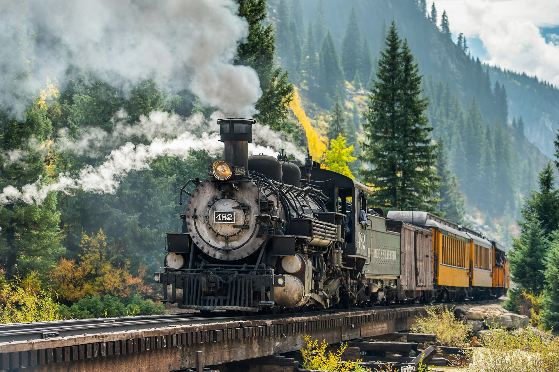 A steam train follows a scenic rural route