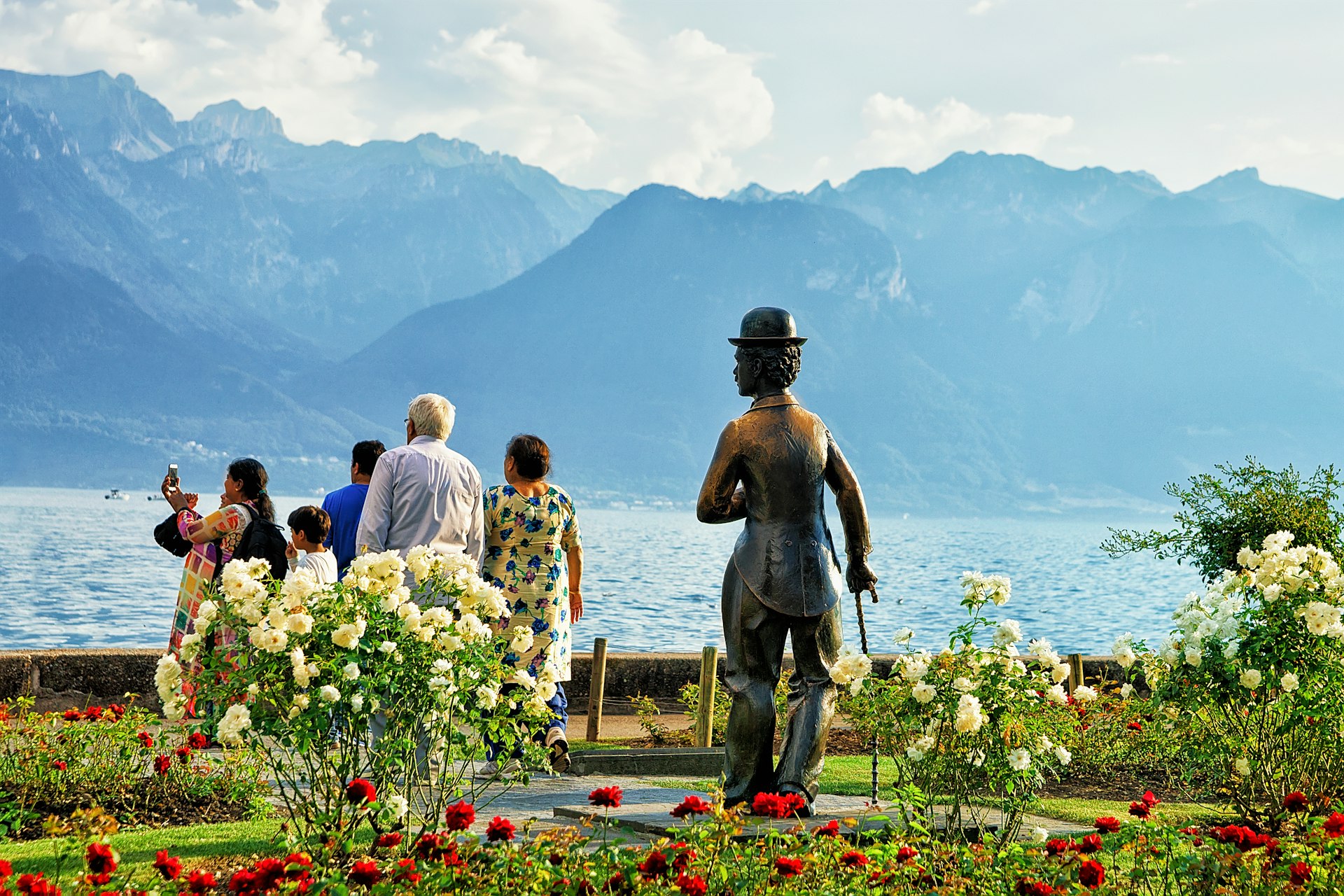 A Charlie Chaplin statue in Vevey overlooks a group of tourists standing in front of Lake Geneva