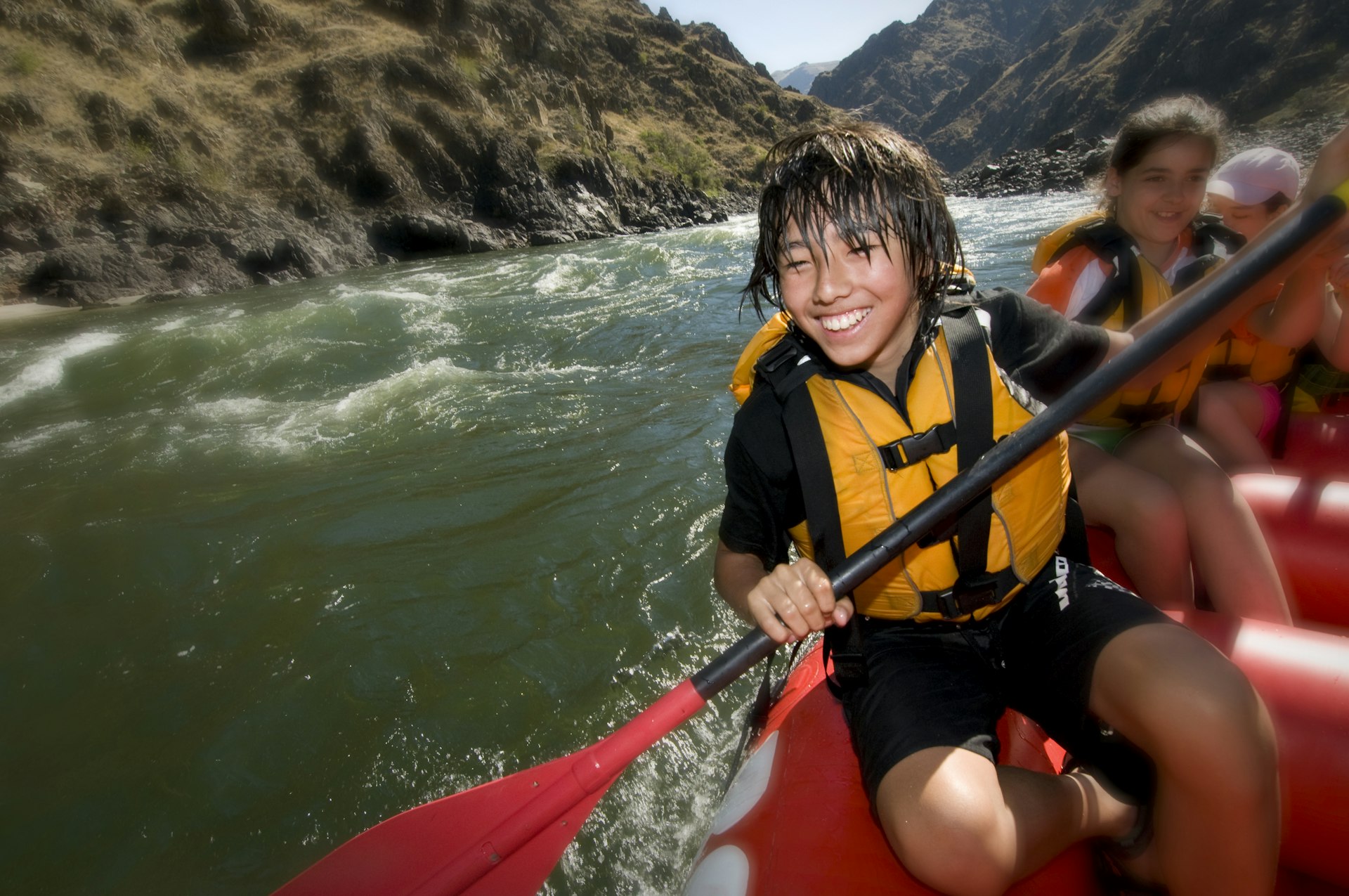 A boy smiles as he rows in a whitewater raft down a canyon river in the USA