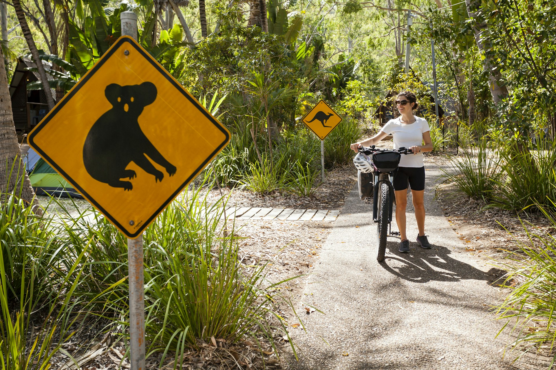 Woman pushing an ebike along a path with two wildlife signs indicating that kangaroos and koalas are in the area