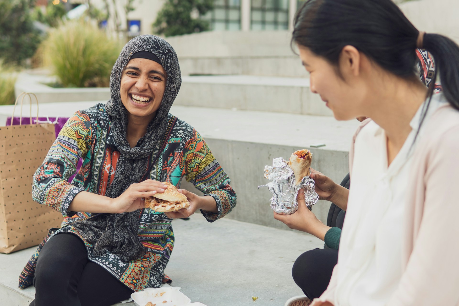 A candid photograph of a Gen Z Muslim woman laughing with friends while out shopping and having a bite to eat in the city.