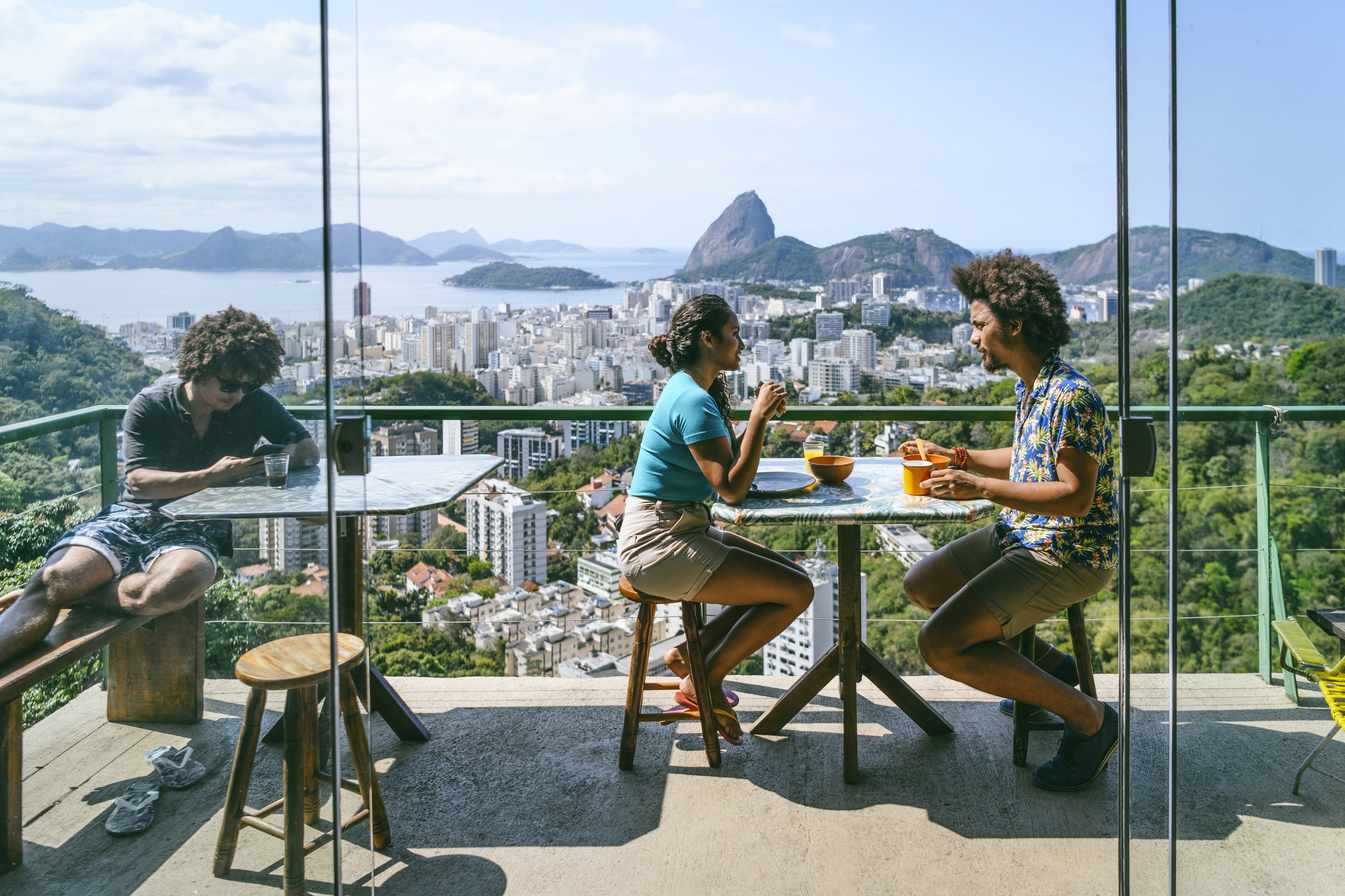 A man and a woman on a balcony, with a scenic view of the city and coastline in the background