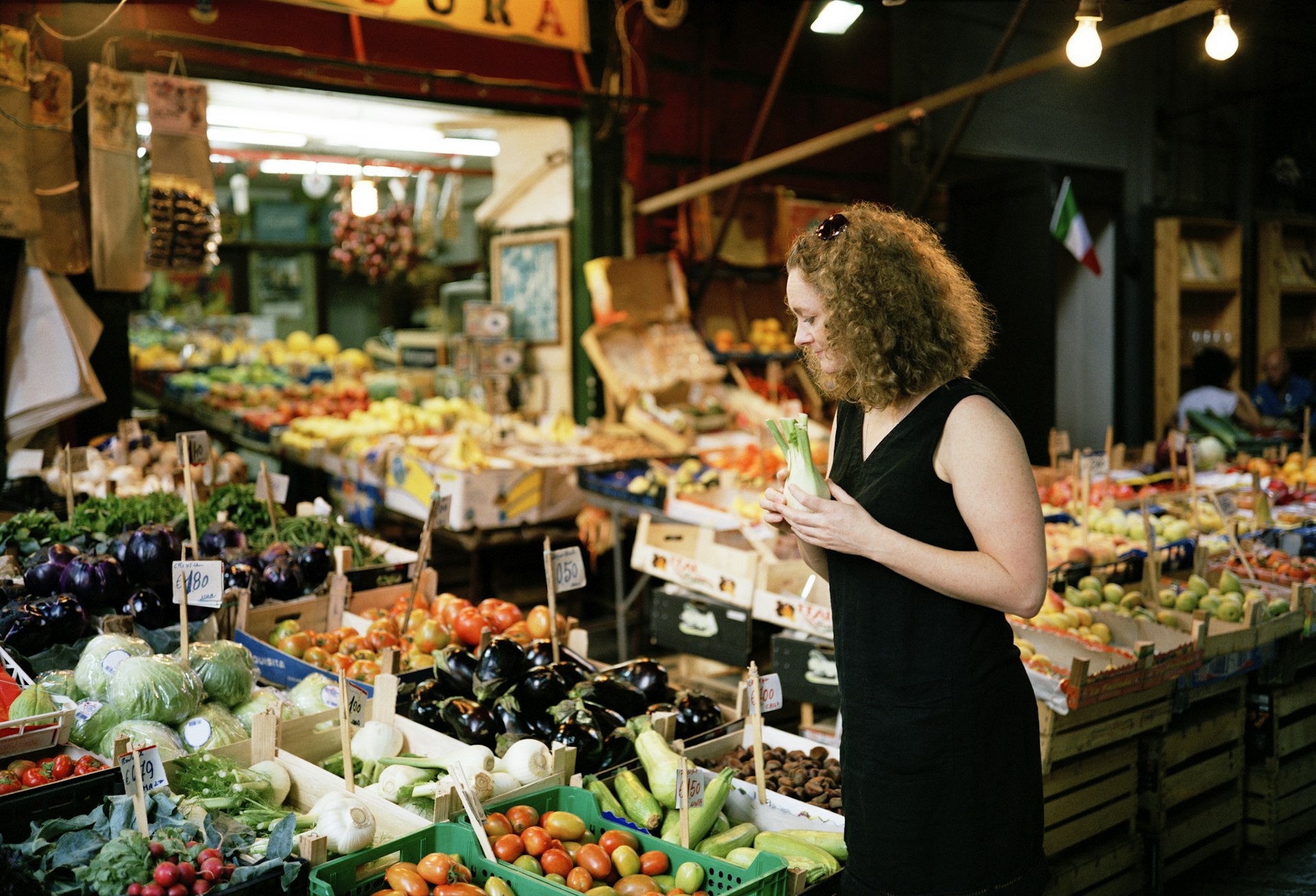 A woman in a black dress looks at the fresh proudce on a market stall in Sicily 