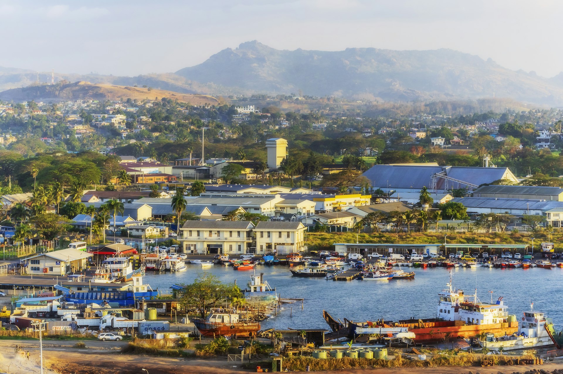 An aerial view of Lautoka, Fiji, with buildings and a harbor in the foreground and a mountain in the background