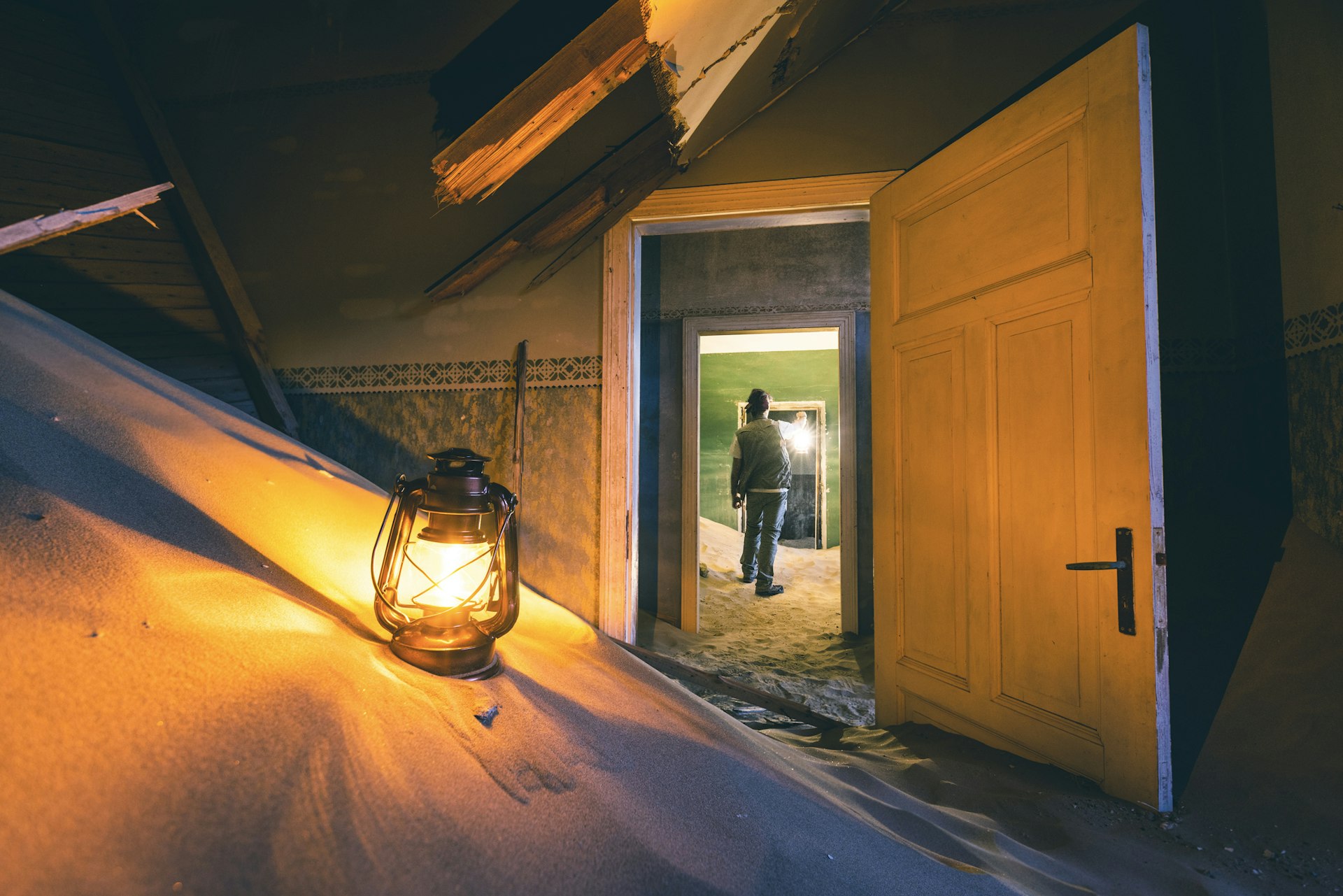 One man with a lantern exploring an abandoned building filled with sand